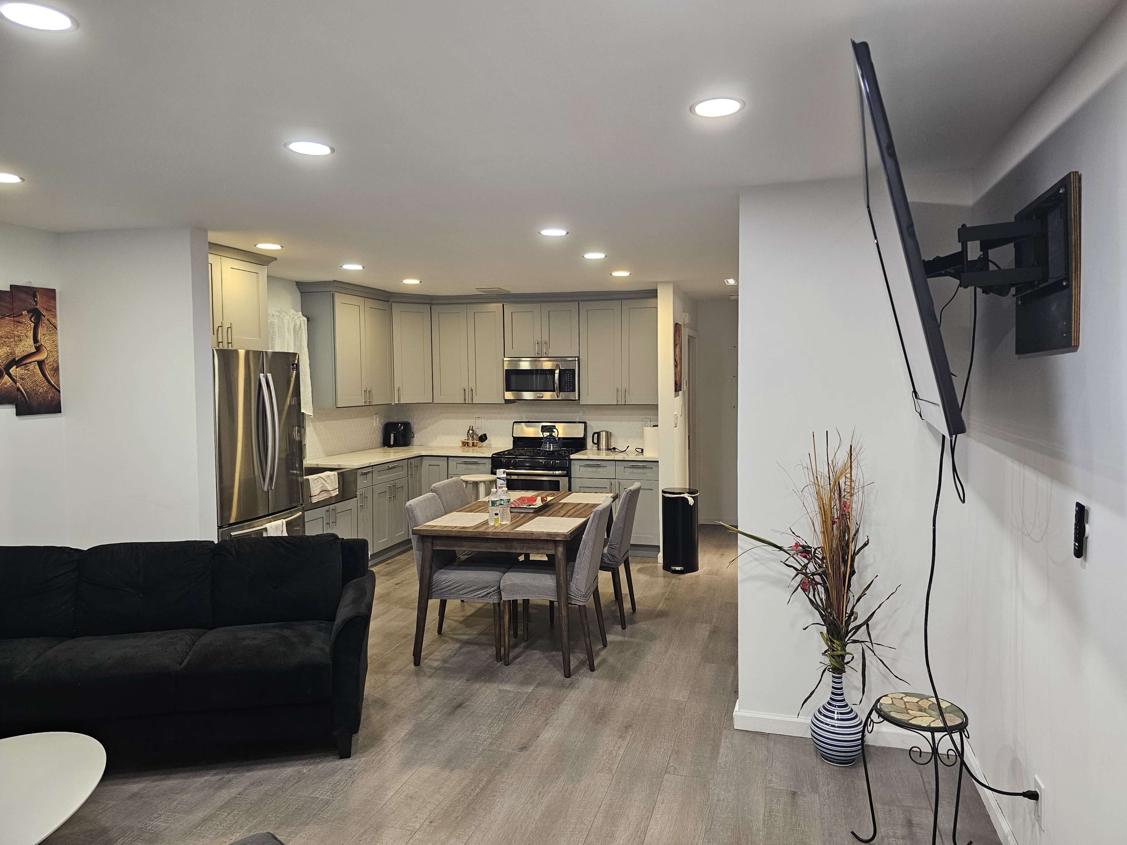 A modern kitchen and living area features a dark couch, a dining table, and stainless steel appliances.