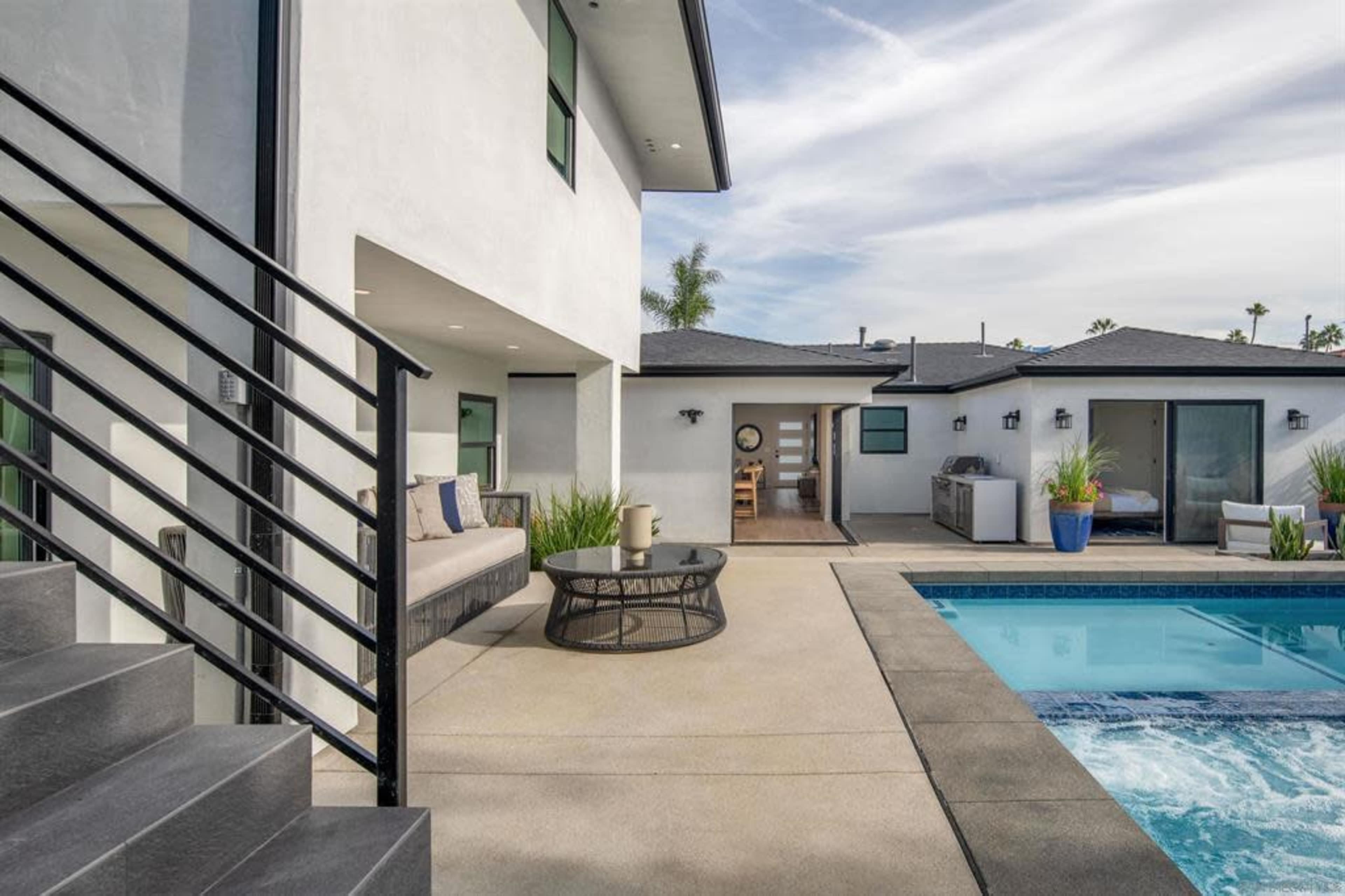 A modern outdoor space features a pool, patio furniture, and a view of a home with large windows.