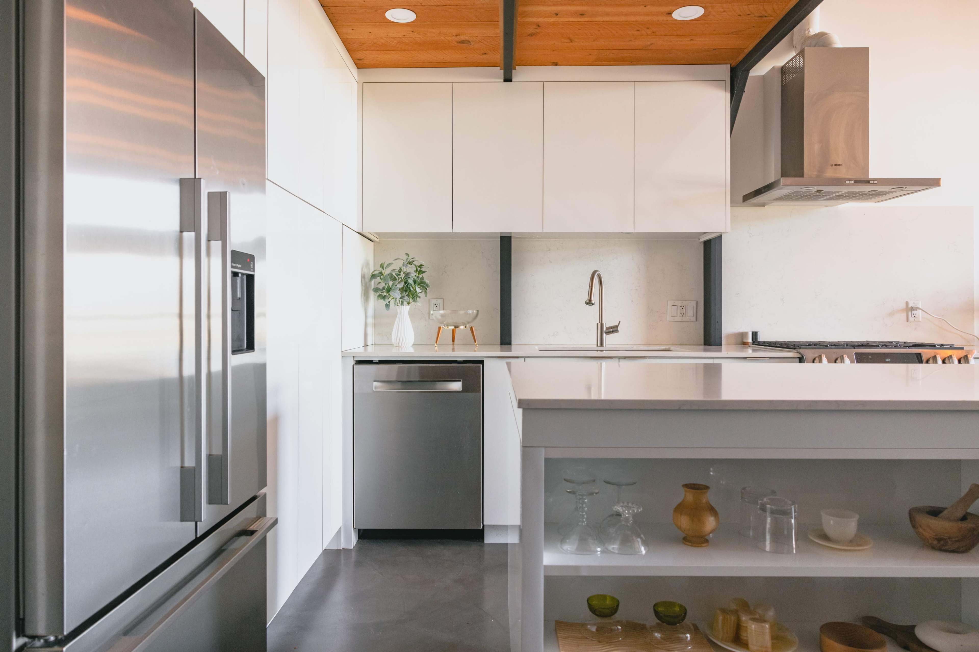 A modern kitchen features stainless steel appliances, white cabinetry, and a wood-paneled ceiling.