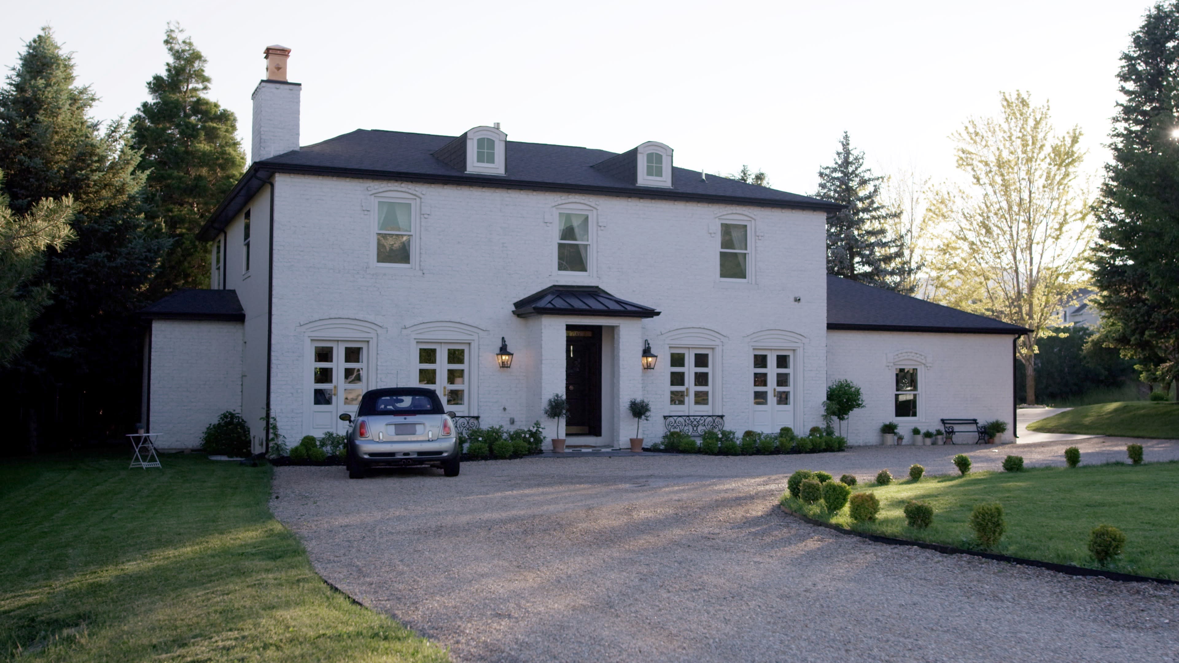 A two-story white house with a gravel driveway and a parked car in front.