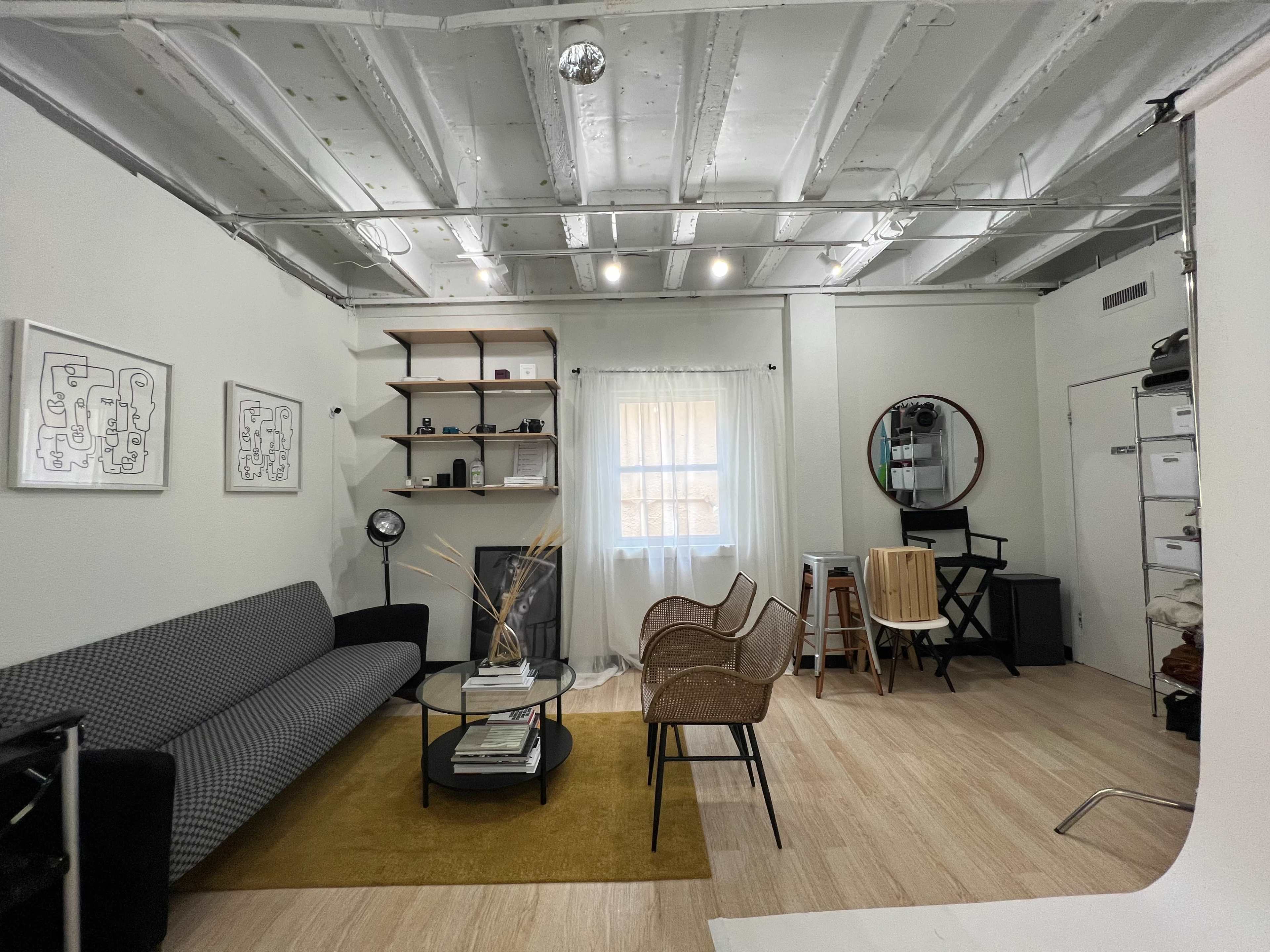 A modern living area with a gray couch, a round glass coffee table, a rug, and various furniture items including chairs and shelves against the walls.