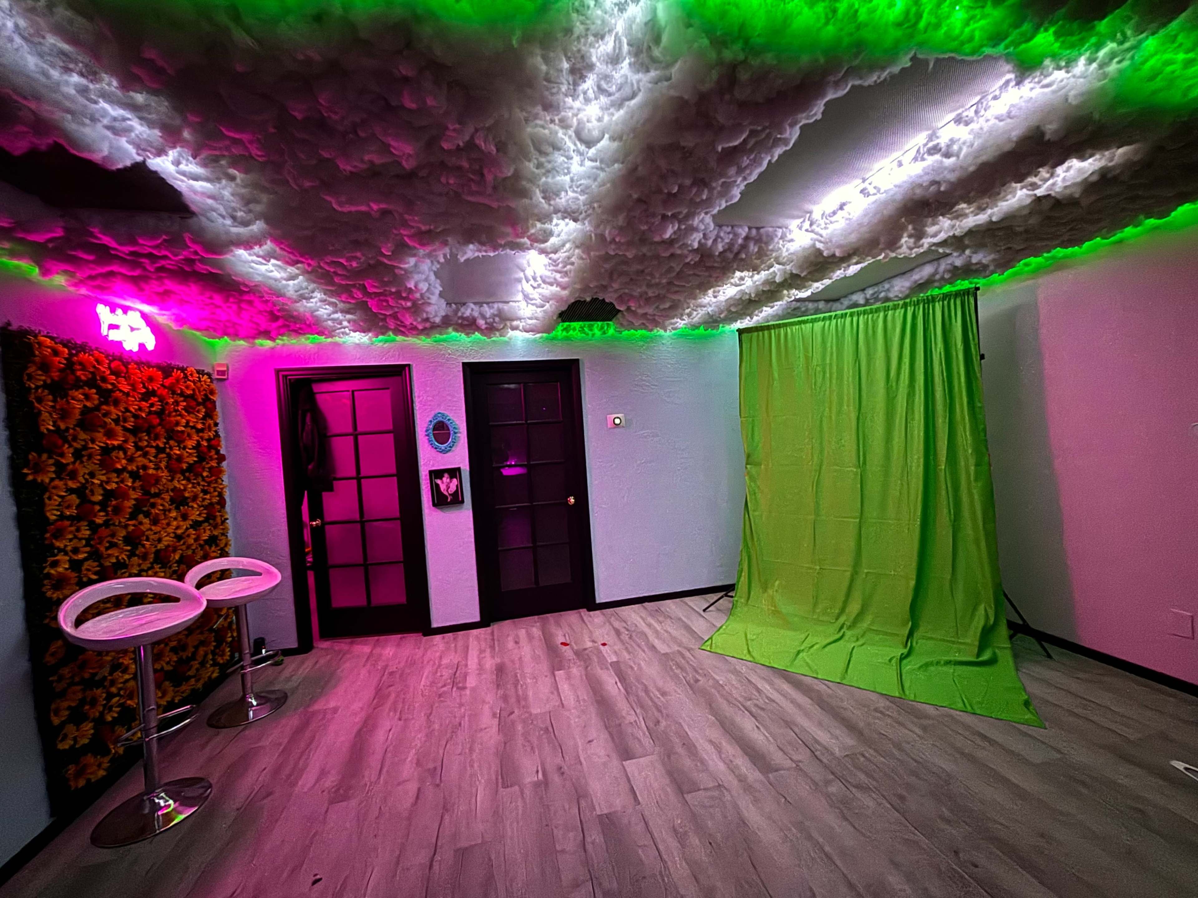 The image shows a room with a textured ceiling illuminated by colorful lighting, a green backdrop, two bar stools, and dual black doors.