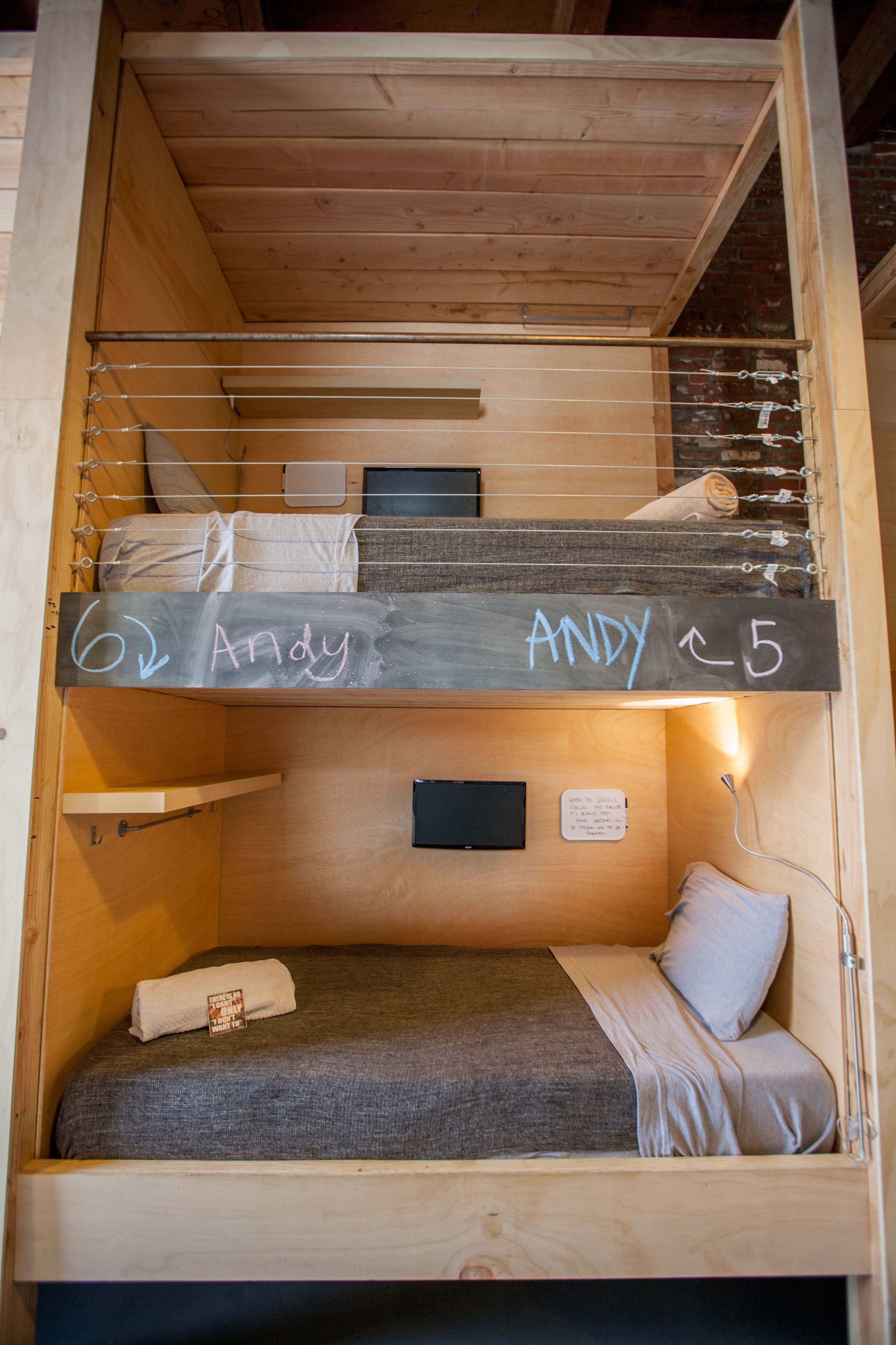 A wooden bunk bed setup with two sleeping areas, one above the other, featuring a minimalist design and a small shelf beside each bed.