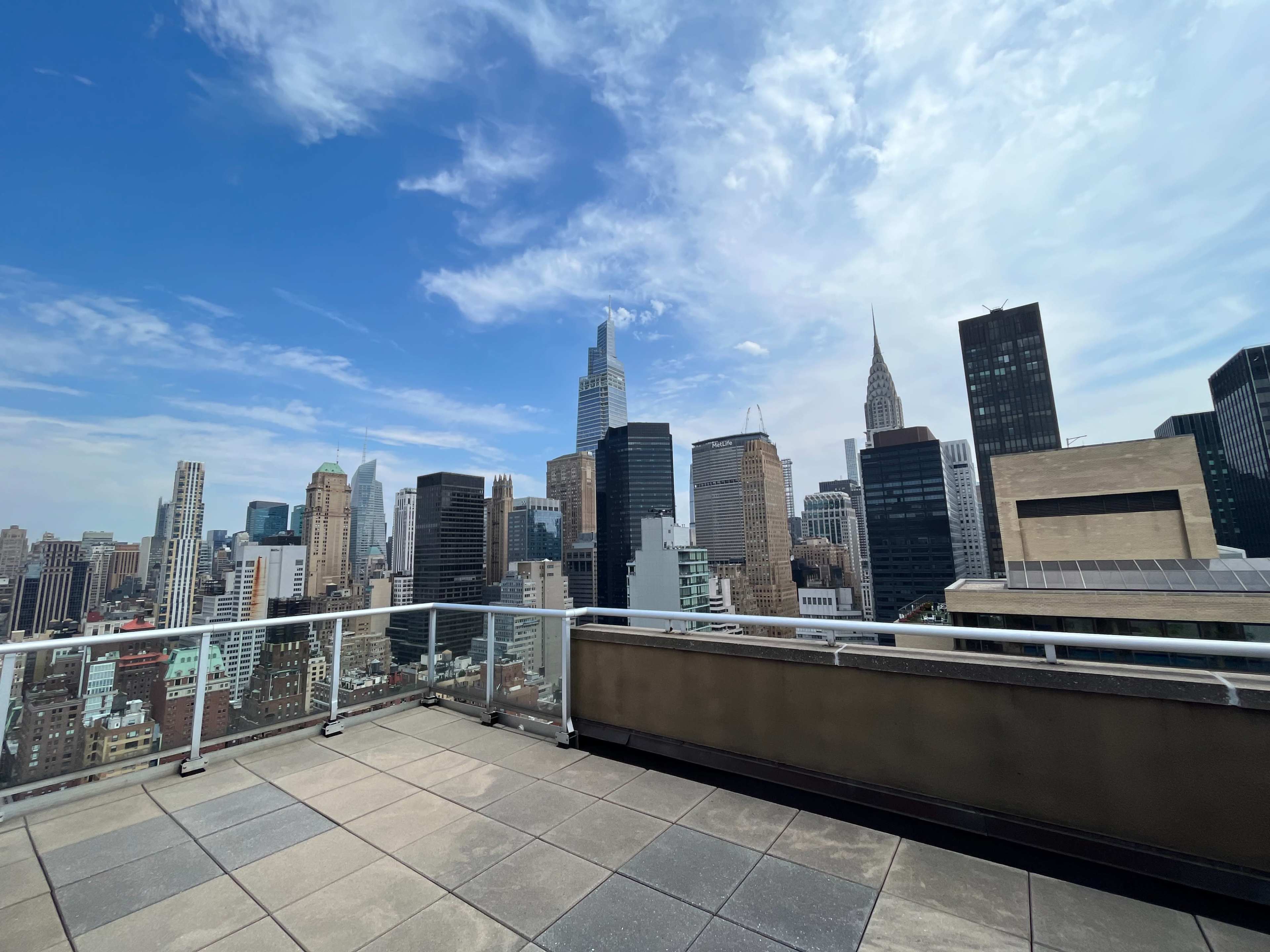 The image shows a rooftop view of a city skyline featuring various skyscrapers under a partly cloudy sky.