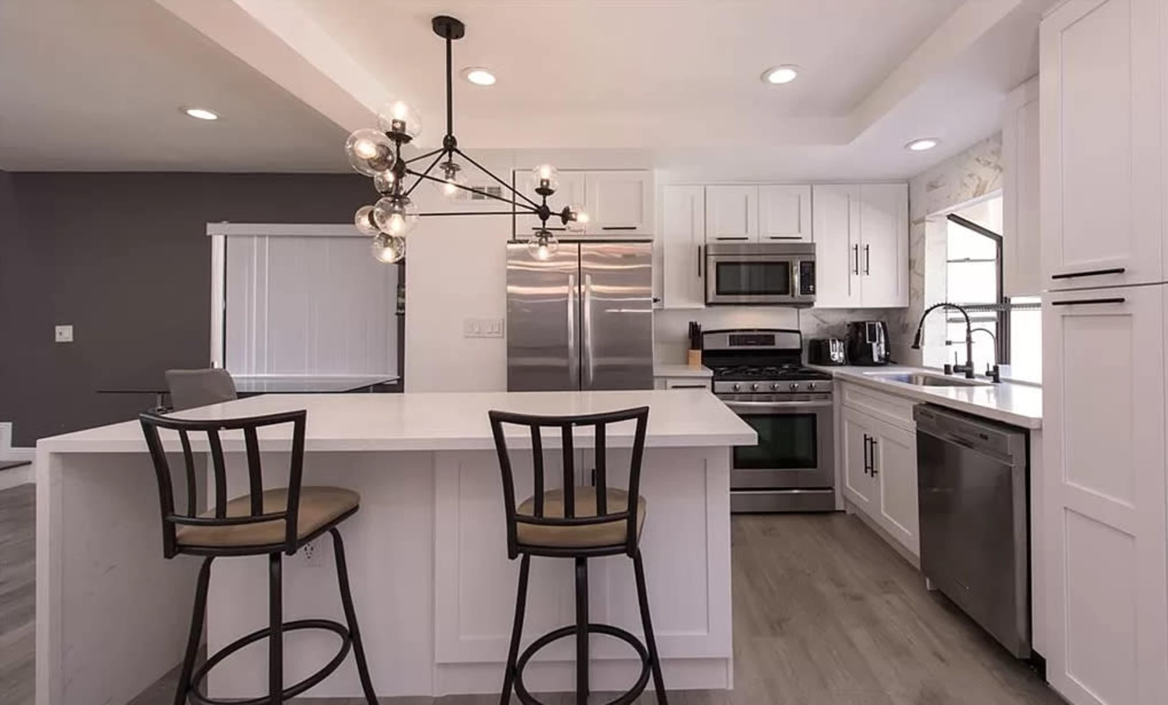 A modern kitchen with white cabinetry, stainless steel appliances, and a central island with two bar stools.