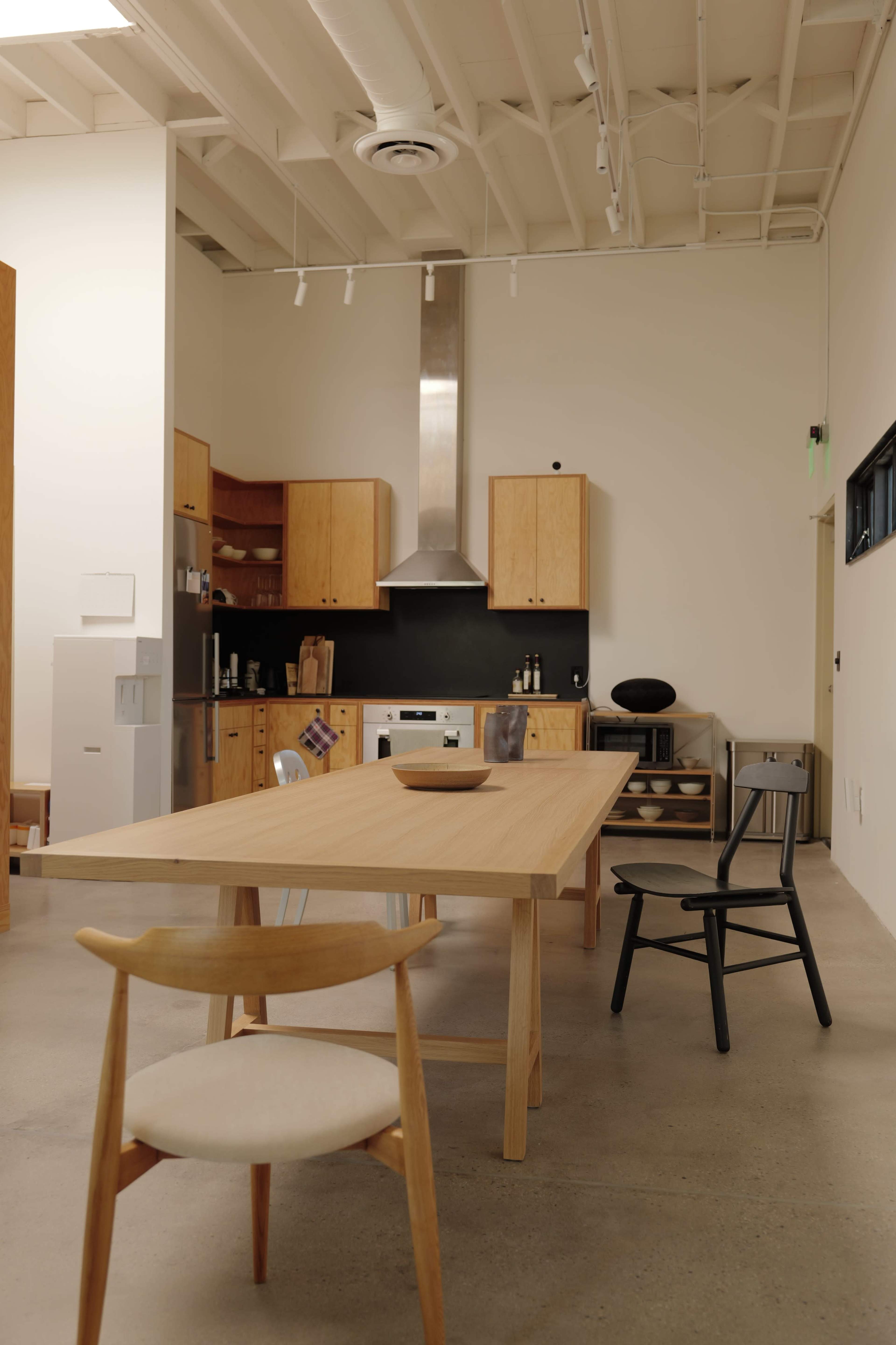 A spacious kitchen-dining area features a wooden table with minimalist chairs, light wood cabinetry, and stainless steel appliances.