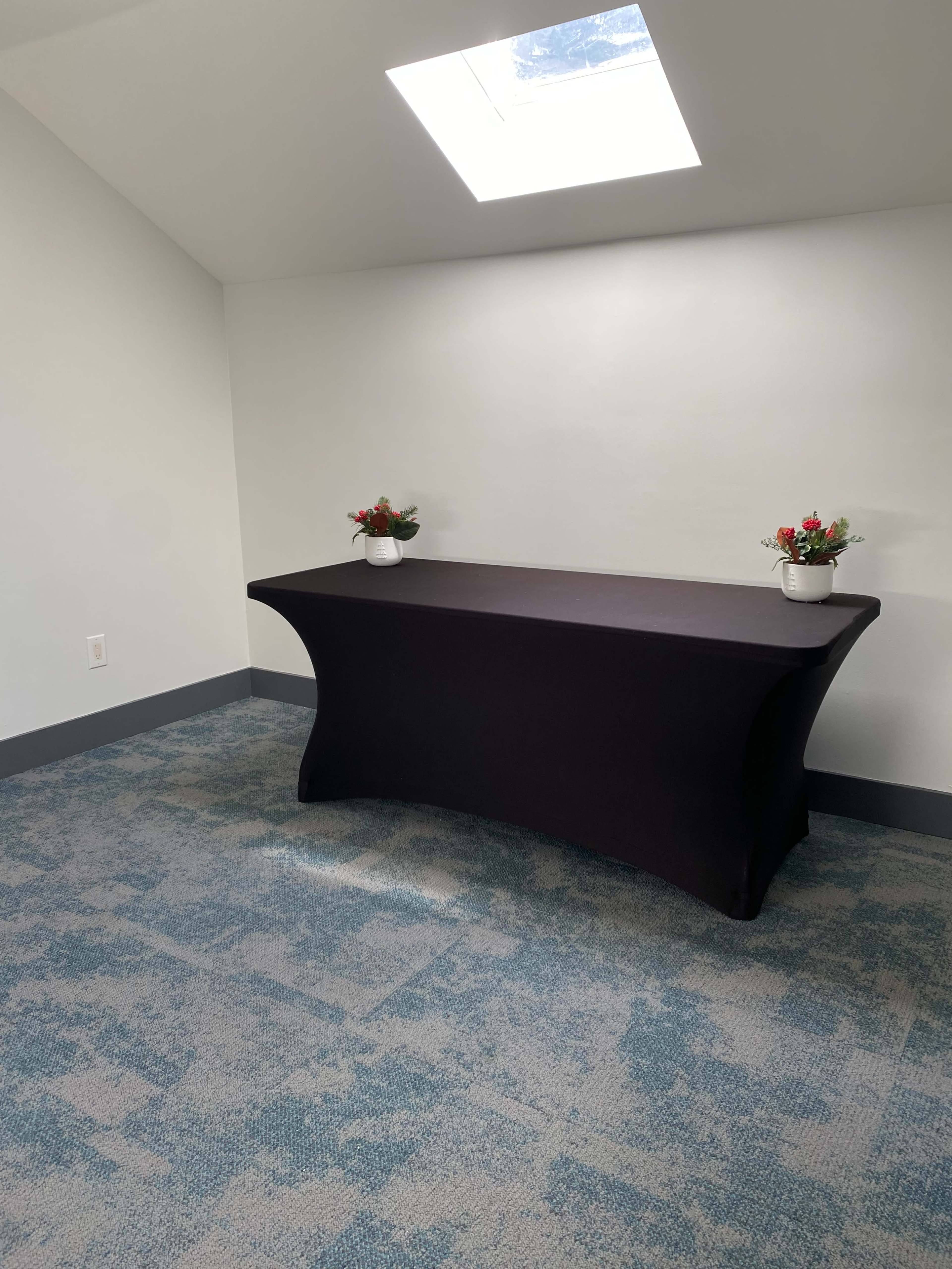 A dark table is set against a light-colored wall in a room with a skylight, featuring two small flower arrangements on top.