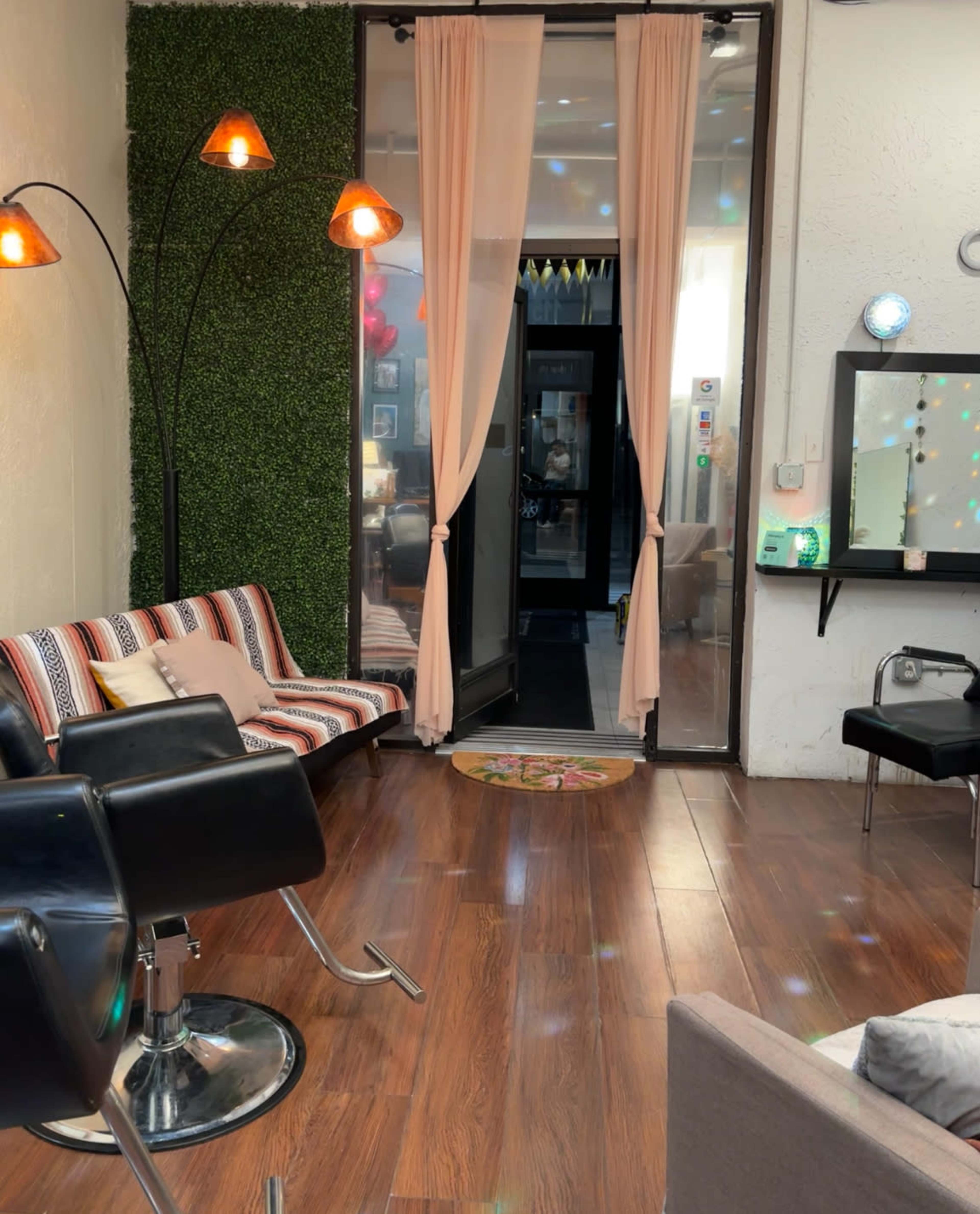 A room with stylish furniture, including a striped couch, black swivel chairs, and large windows with light curtains, leading to an entrance.