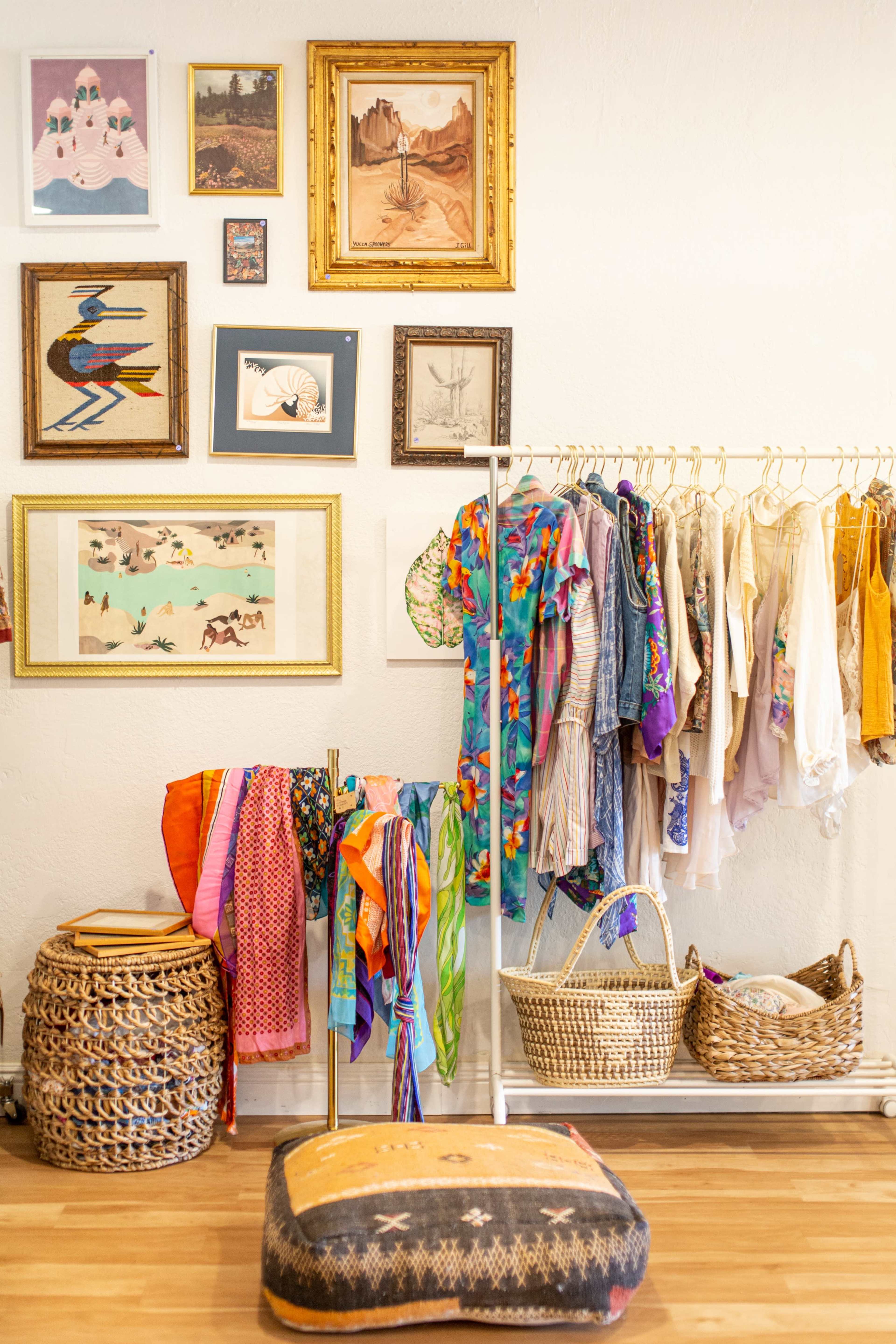 The image shows a boutique interior with a rack of colorful clothing, framed art on the walls, and woven baskets arranged around a floor cushion.