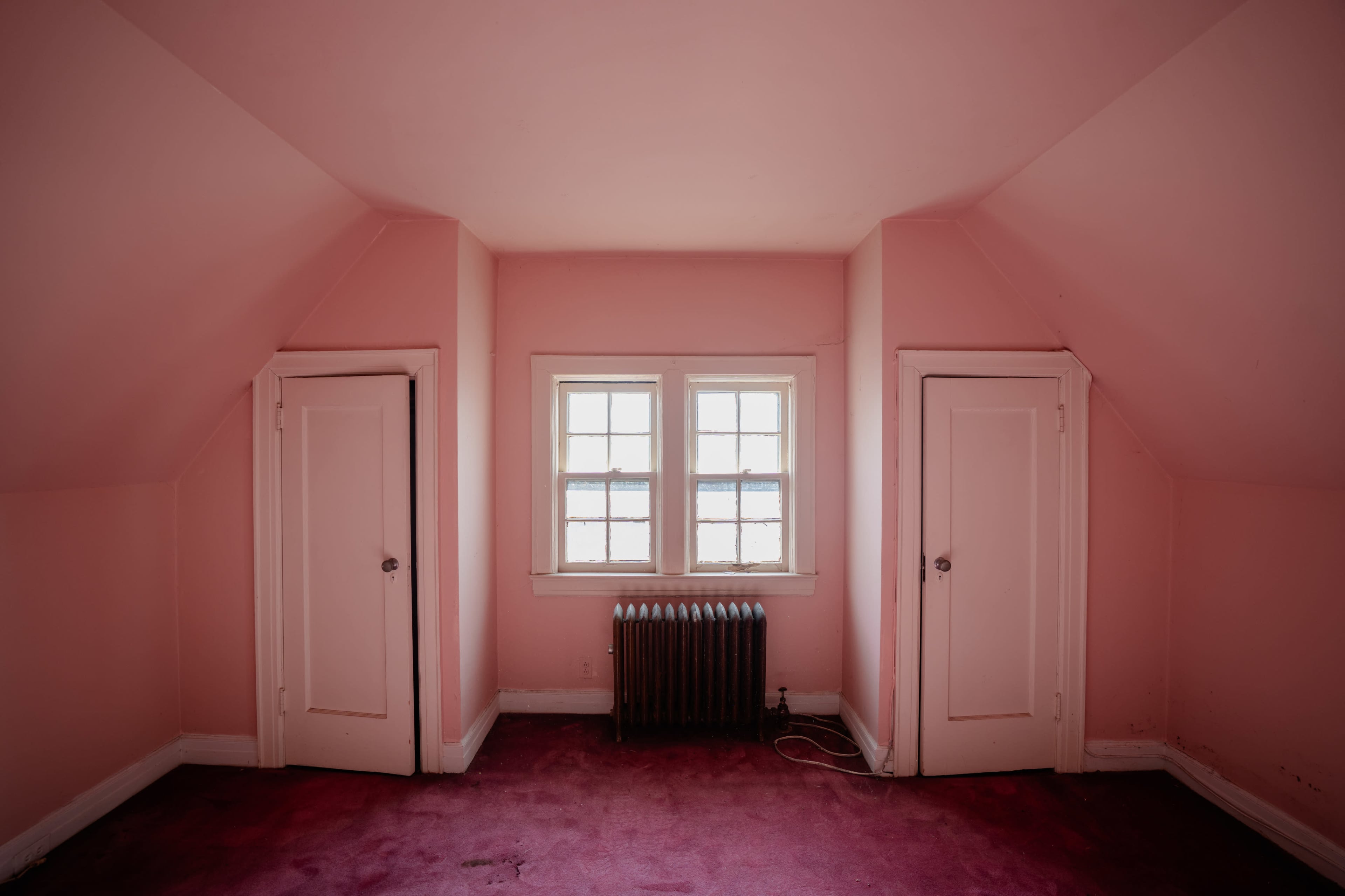 The image shows a pink-walled room with two white doors on either side and a small window in the center.