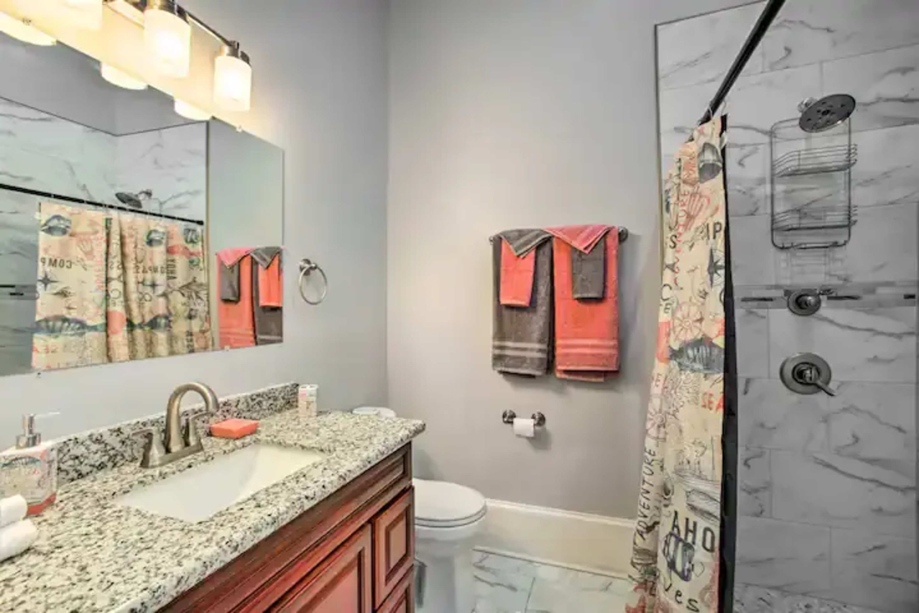 A bathroom featuring a granite countertop, a large mirror, a glass shower, and various towels hanging on a rack.