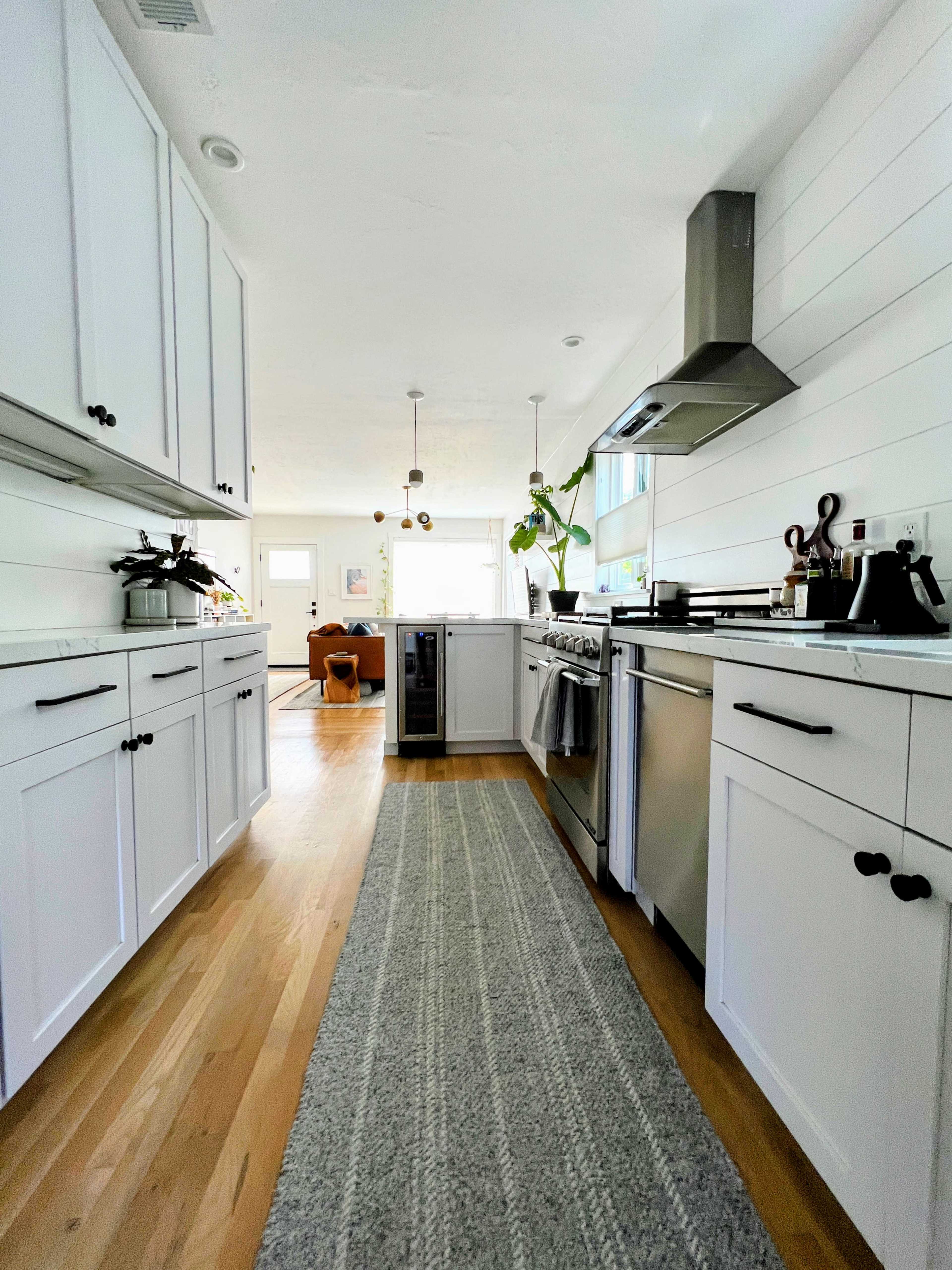 A modern kitchen features white cabinetry, stainless steel appliances, and a rug running down the center.