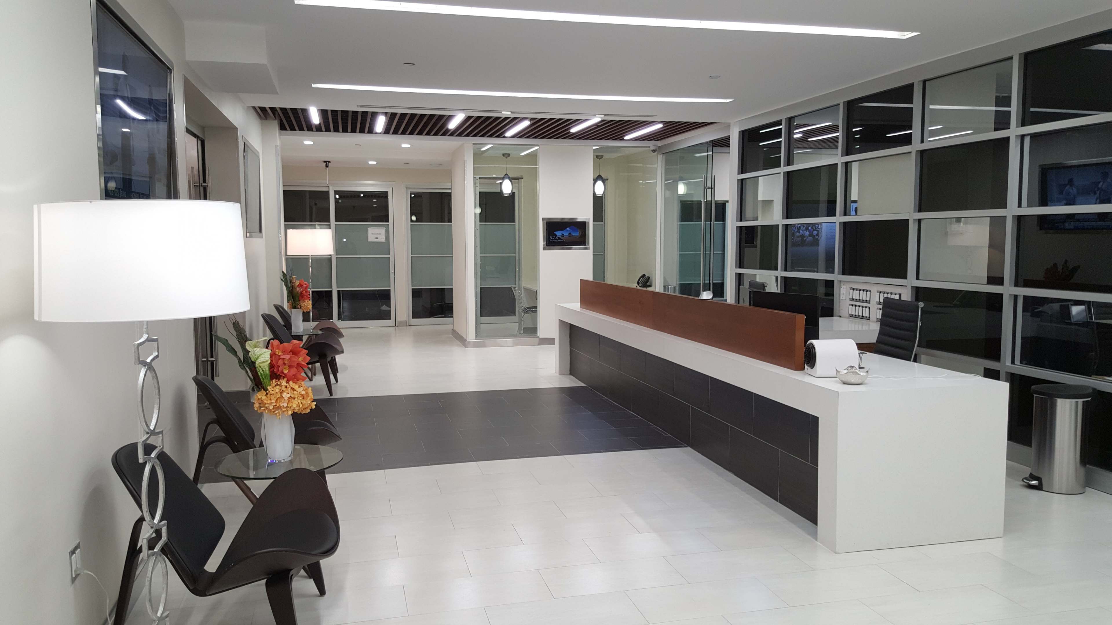 The image shows a modern reception area with a front desk, seating arrangements, and large glass windows.