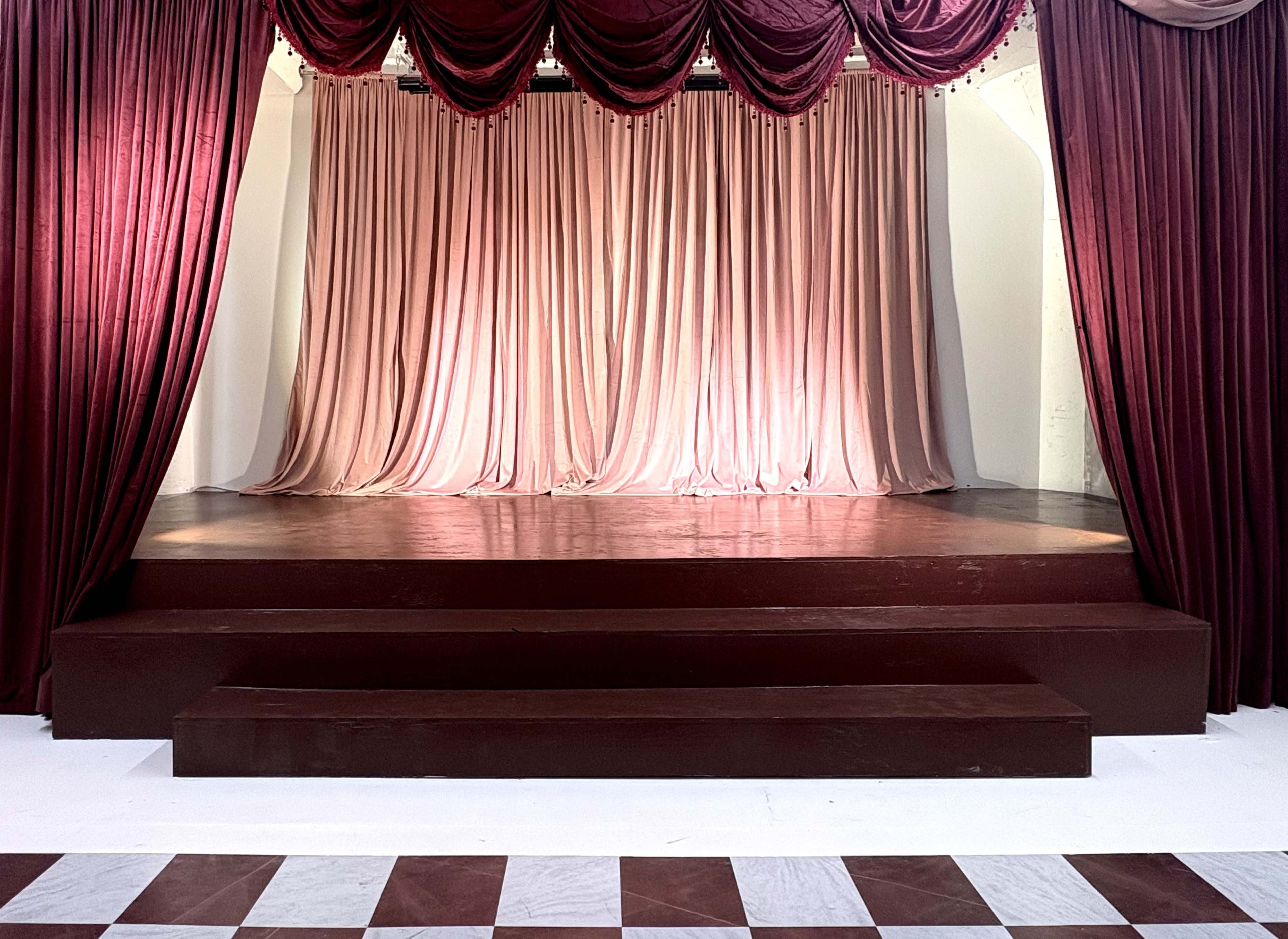 The image shows a stage with a maroon curtain and a raised platform, flanked by draped fabric.