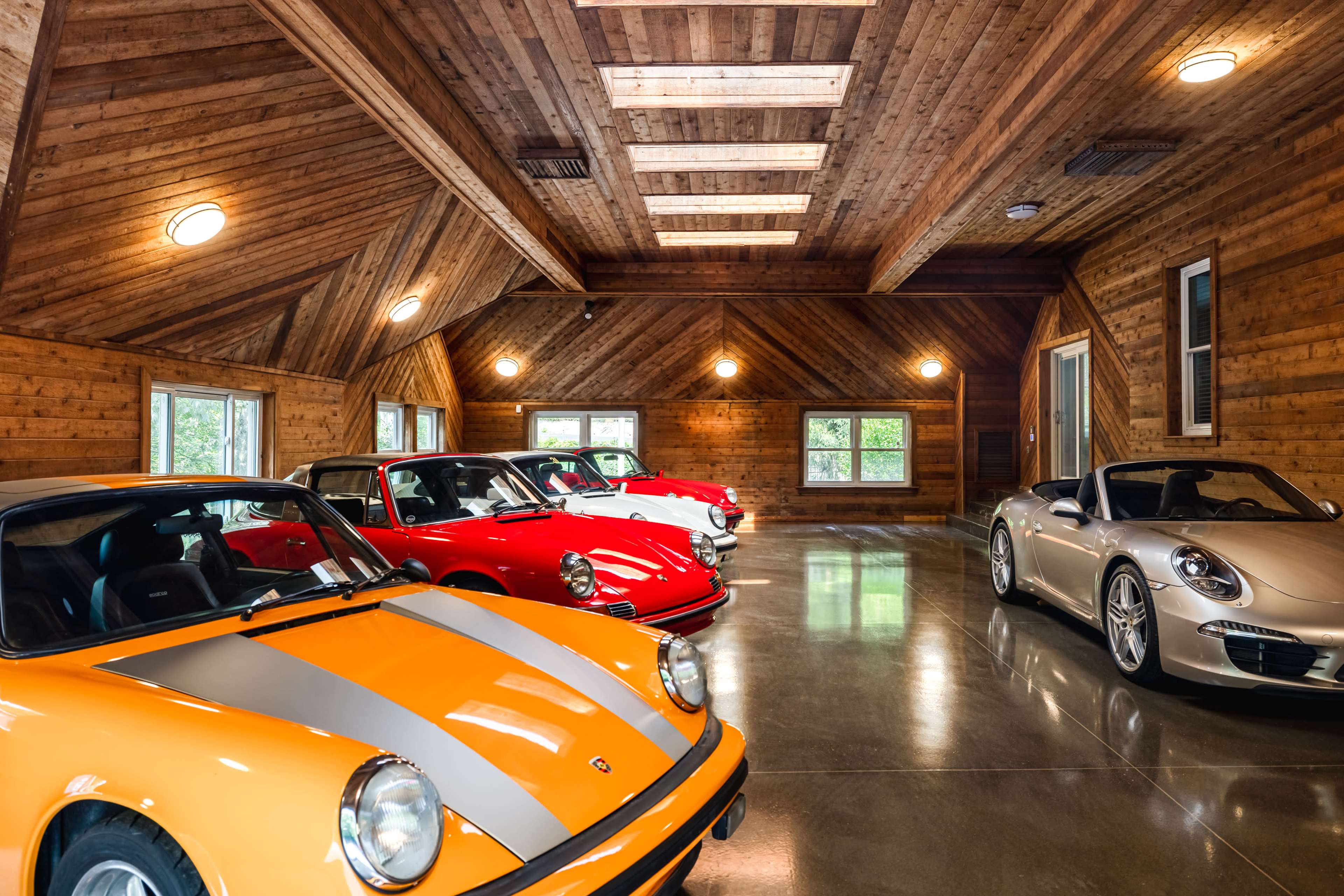 A spacious garage features several vintage and modern Porsche cars lined up under a wooden vaulted ceiling.