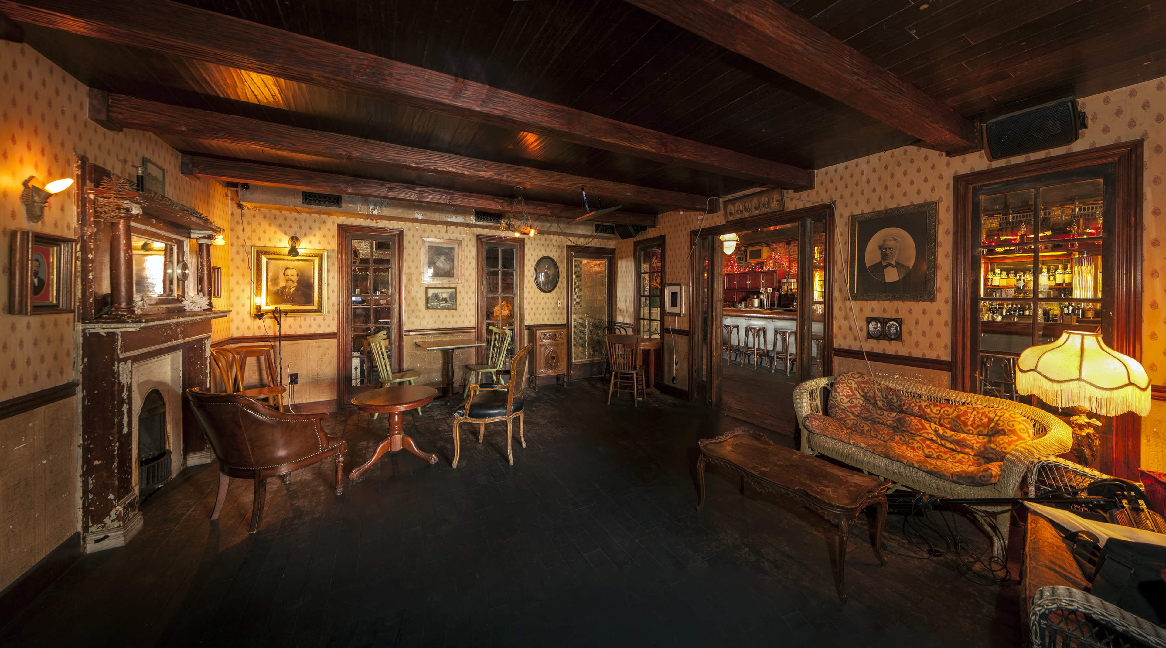 A dimly lit vintage lounge with wooden beams, a fireplace, and various seating arrangements including chairs and a sofa.