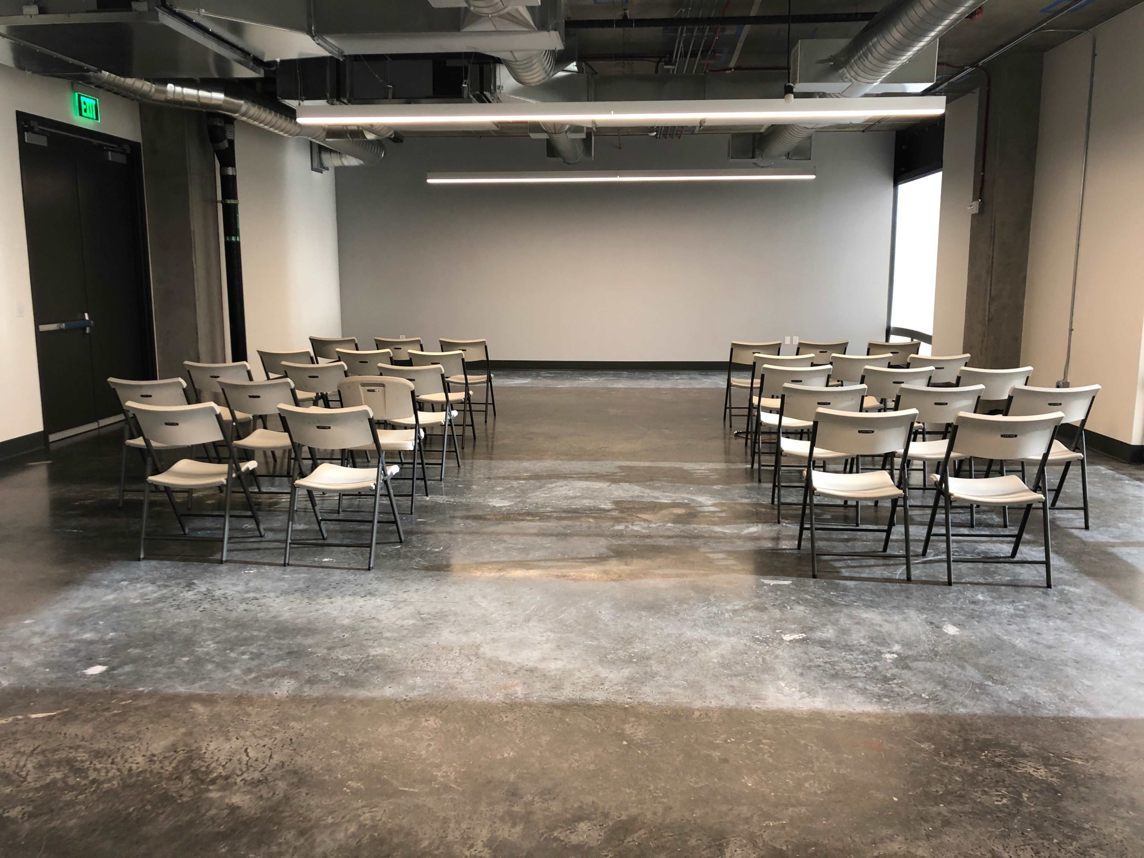 An empty meeting room features rows of gray folding chairs facing a blank wall.