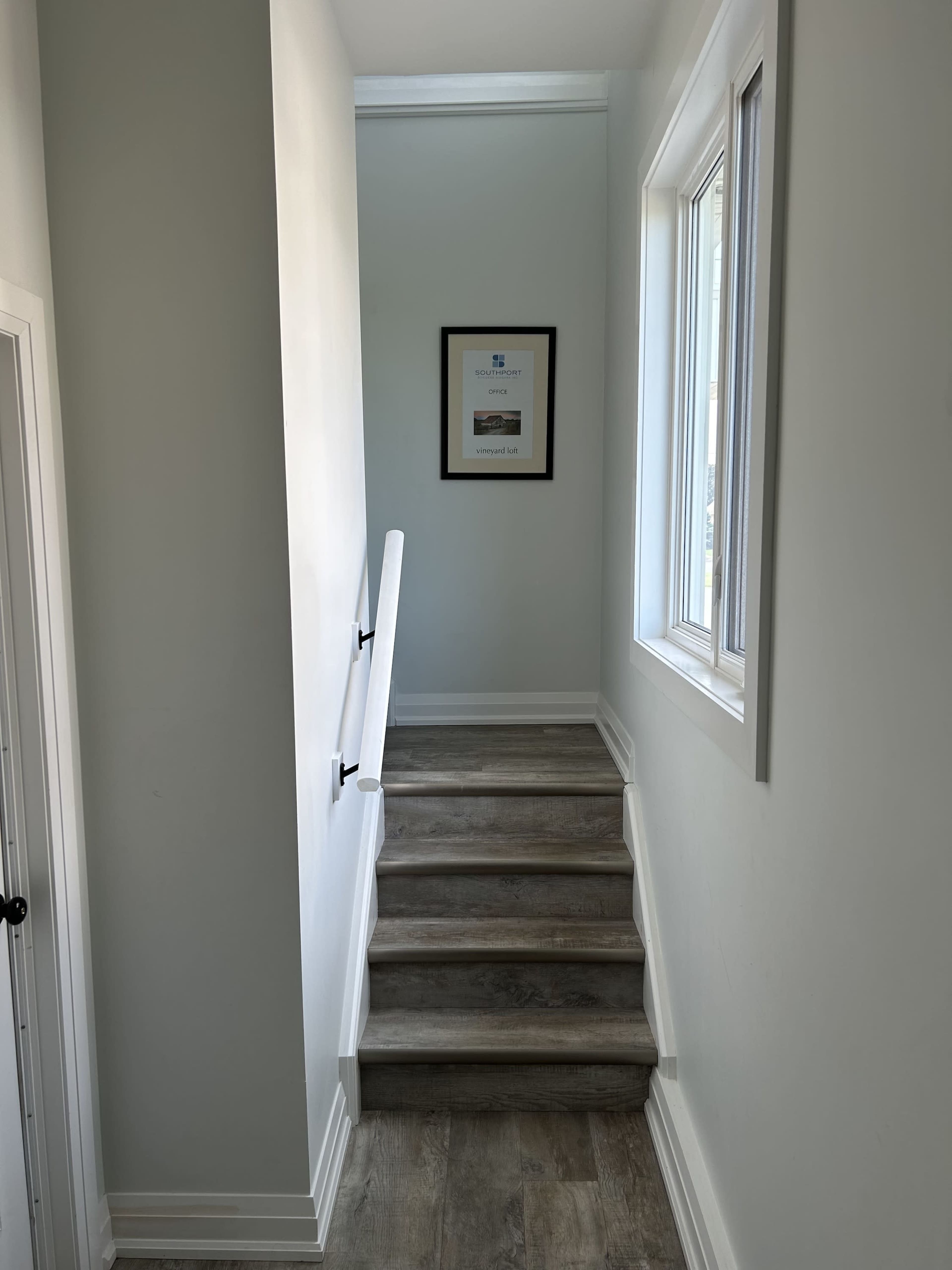 A staircase leading to a well-lit hallway with a framed picture on the wall.
