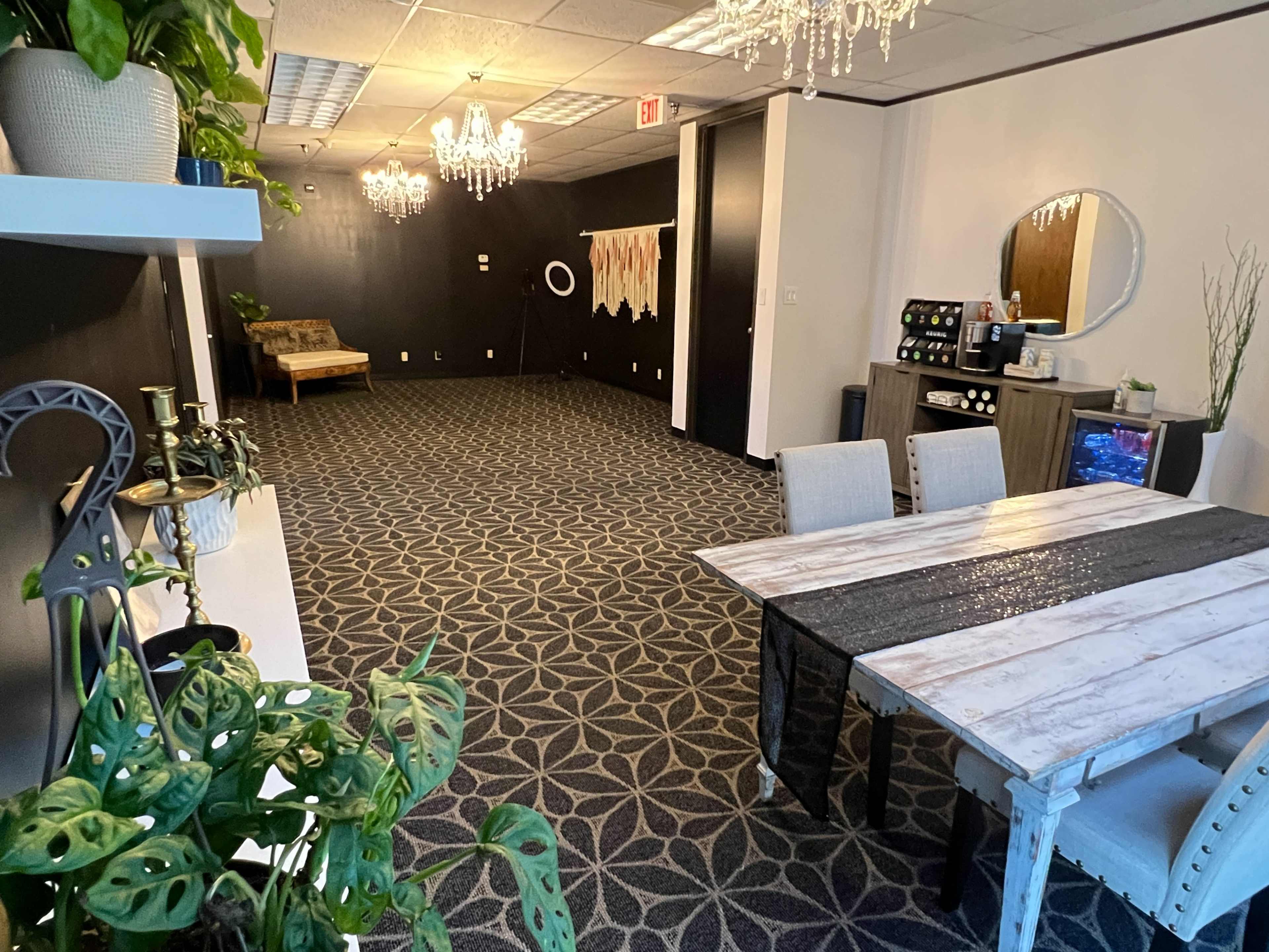 A spacious room with a patterned carpet, a dining table with chairs, and decorative elements like chandeliers and plants.