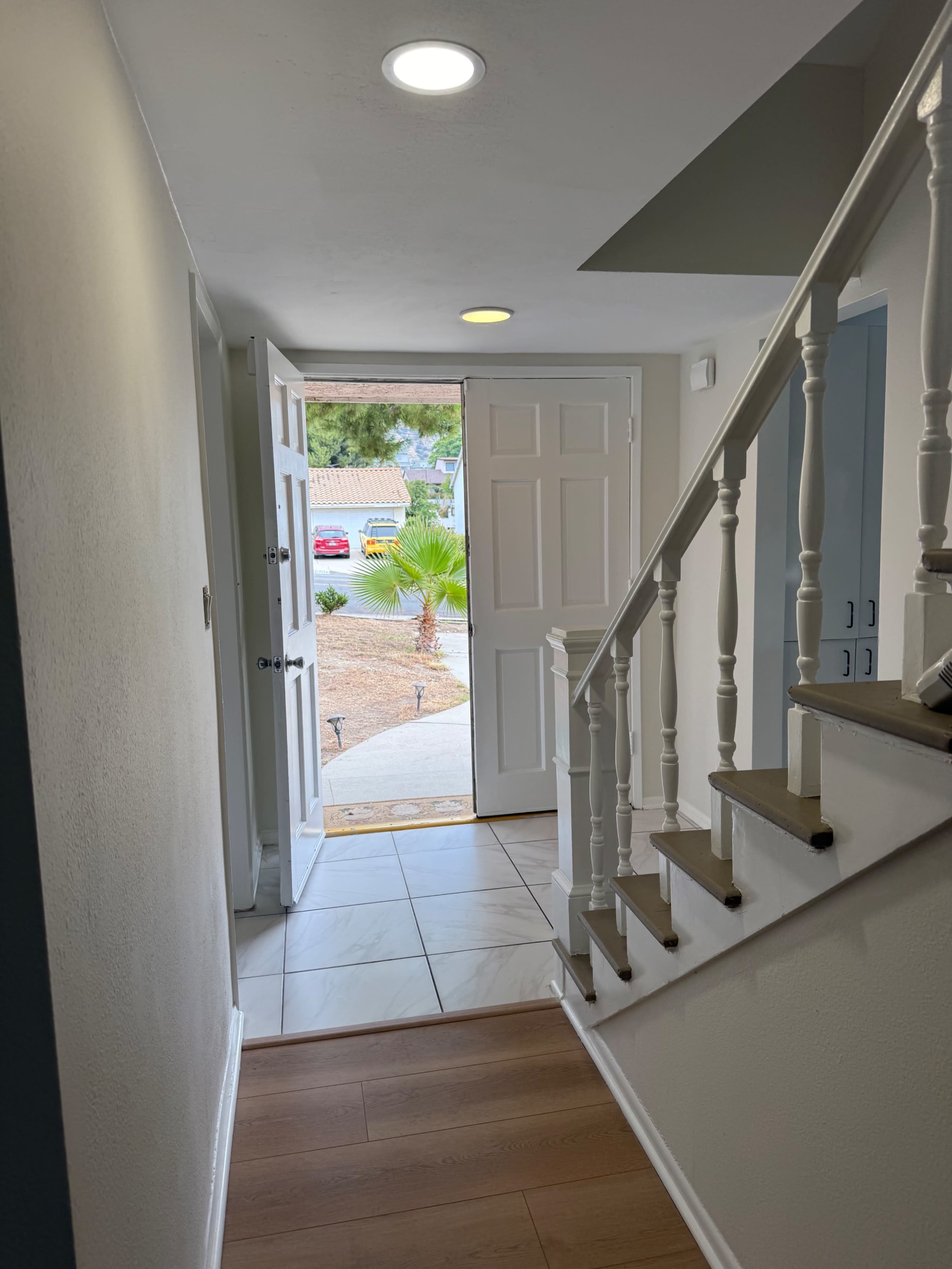 The image shows a well-lit entrance hallway with a staircase on the right and an open door leading outside.