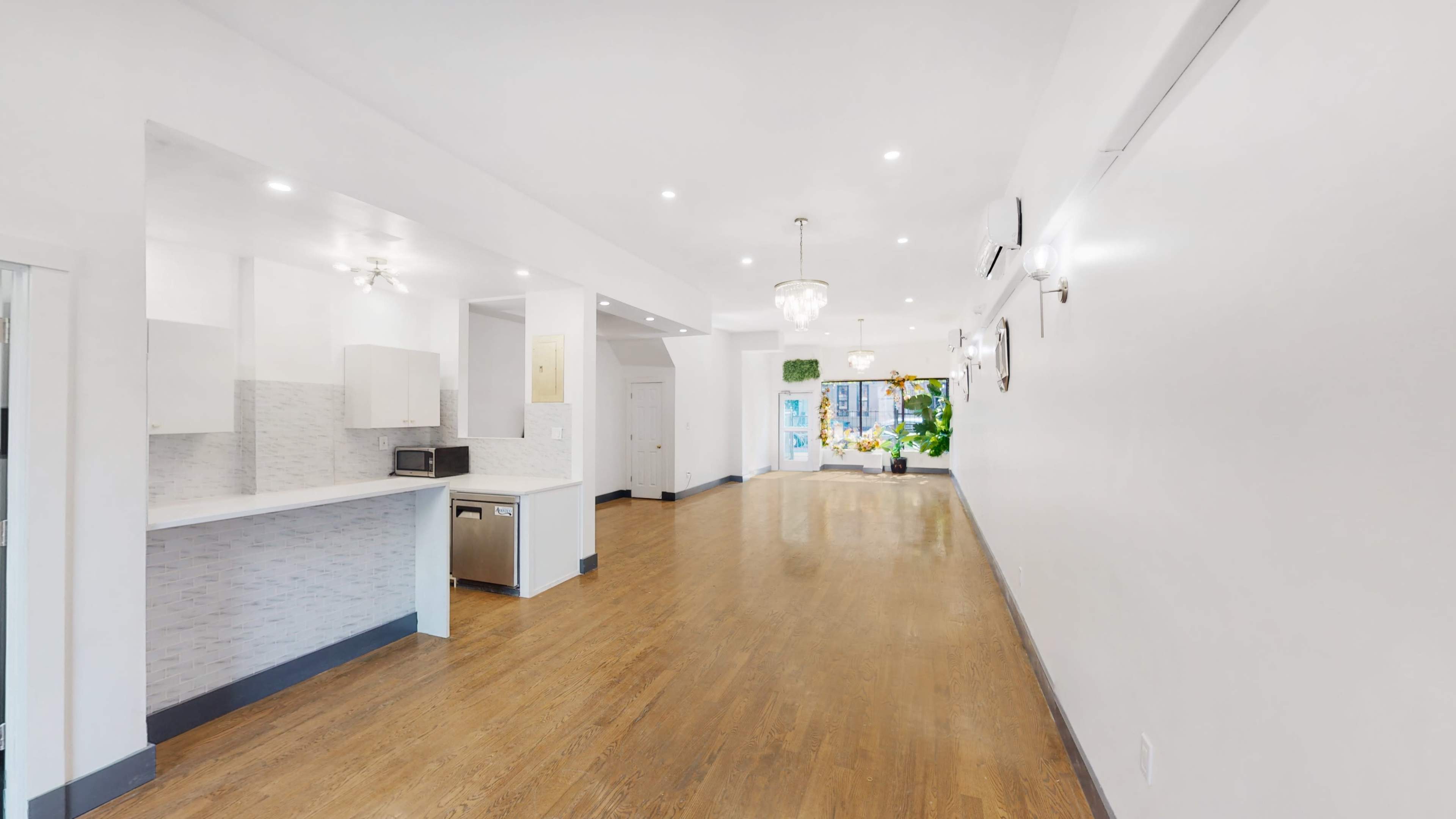 A spacious, modern interior with hardwood floors, white walls, and a view of a bright window at the far end.