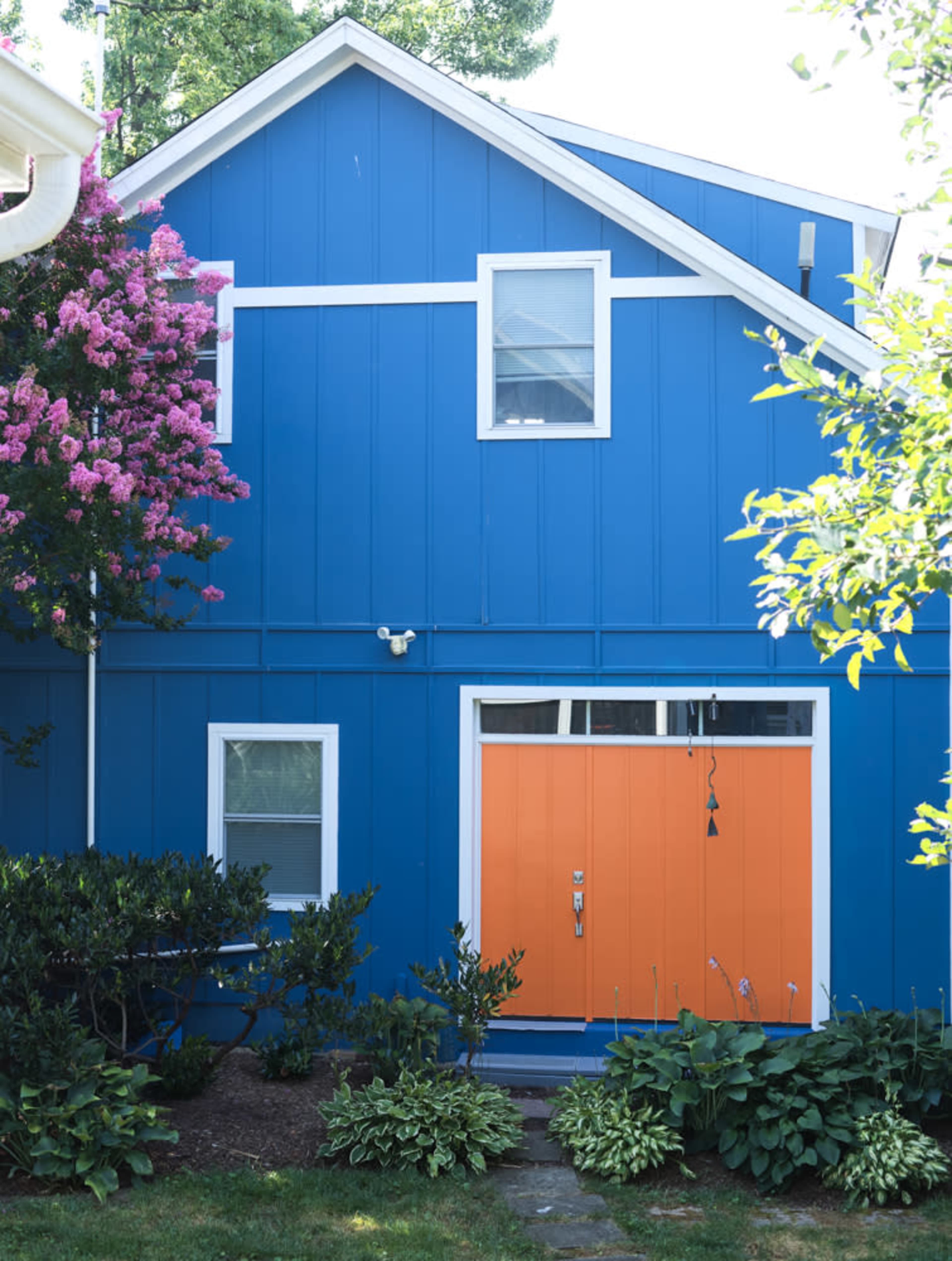 A bright blue house features an orange door and a flowering tree nearby.