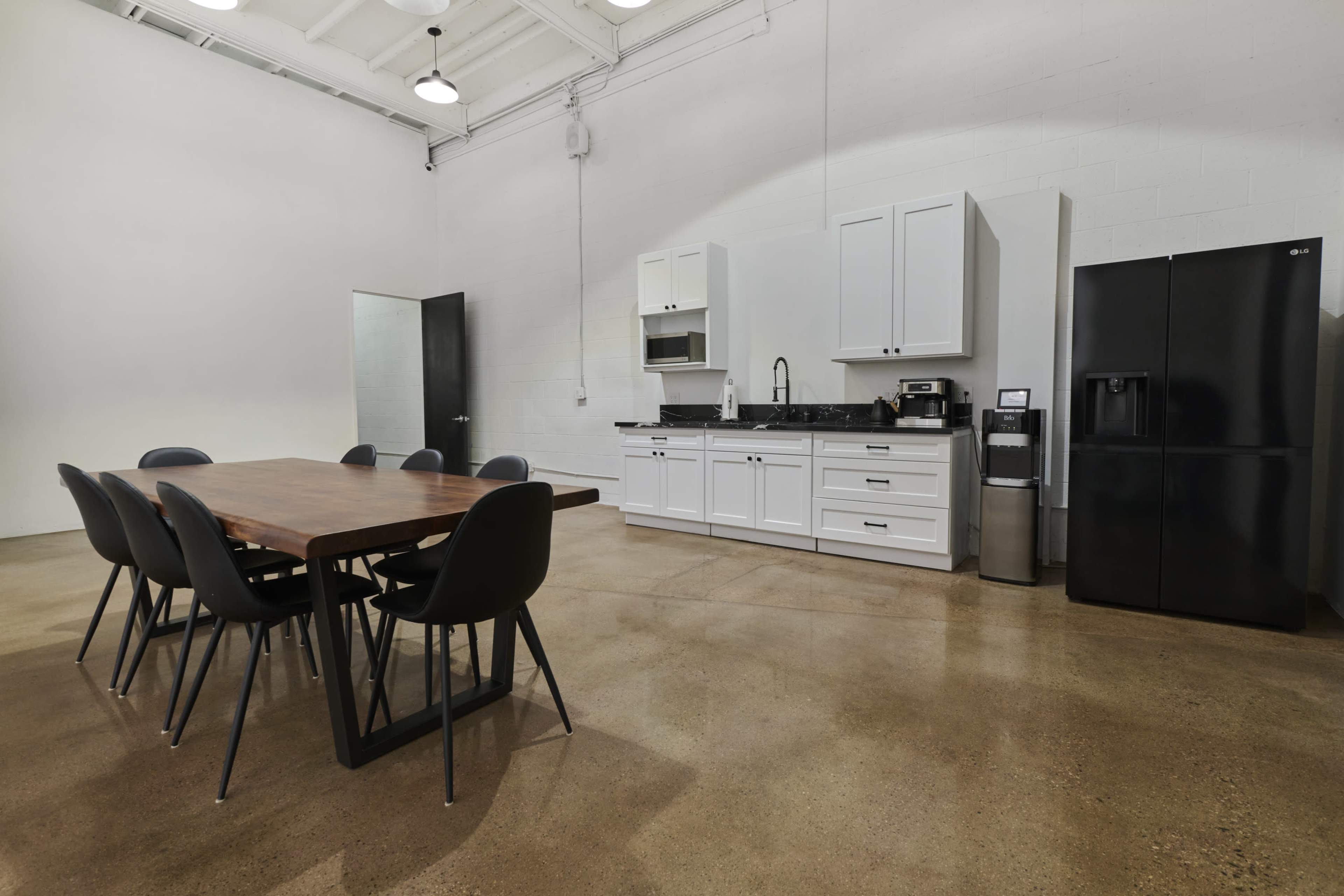 The image shows a modern kitchen area with a dining table and eight chairs, a refrigerator, and a stove against a white wall.