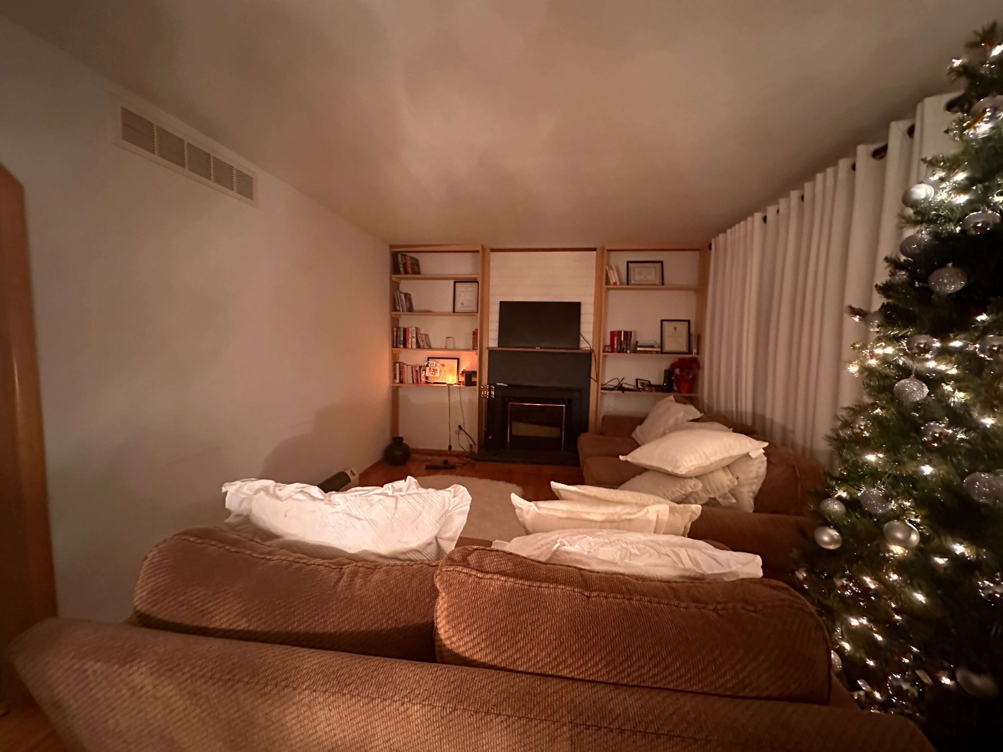 A cozy living room featuring a sofa, a television set against a shelf, and a decorated Christmas tree in the corner.