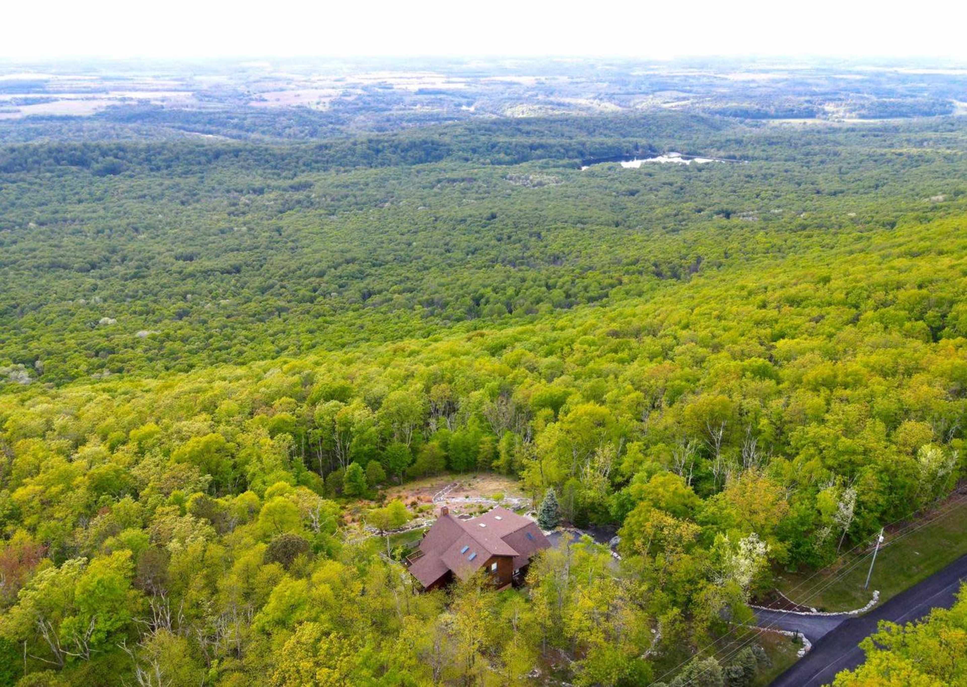 Aerial view of a brown house surrounded by dense green forest and hills.
