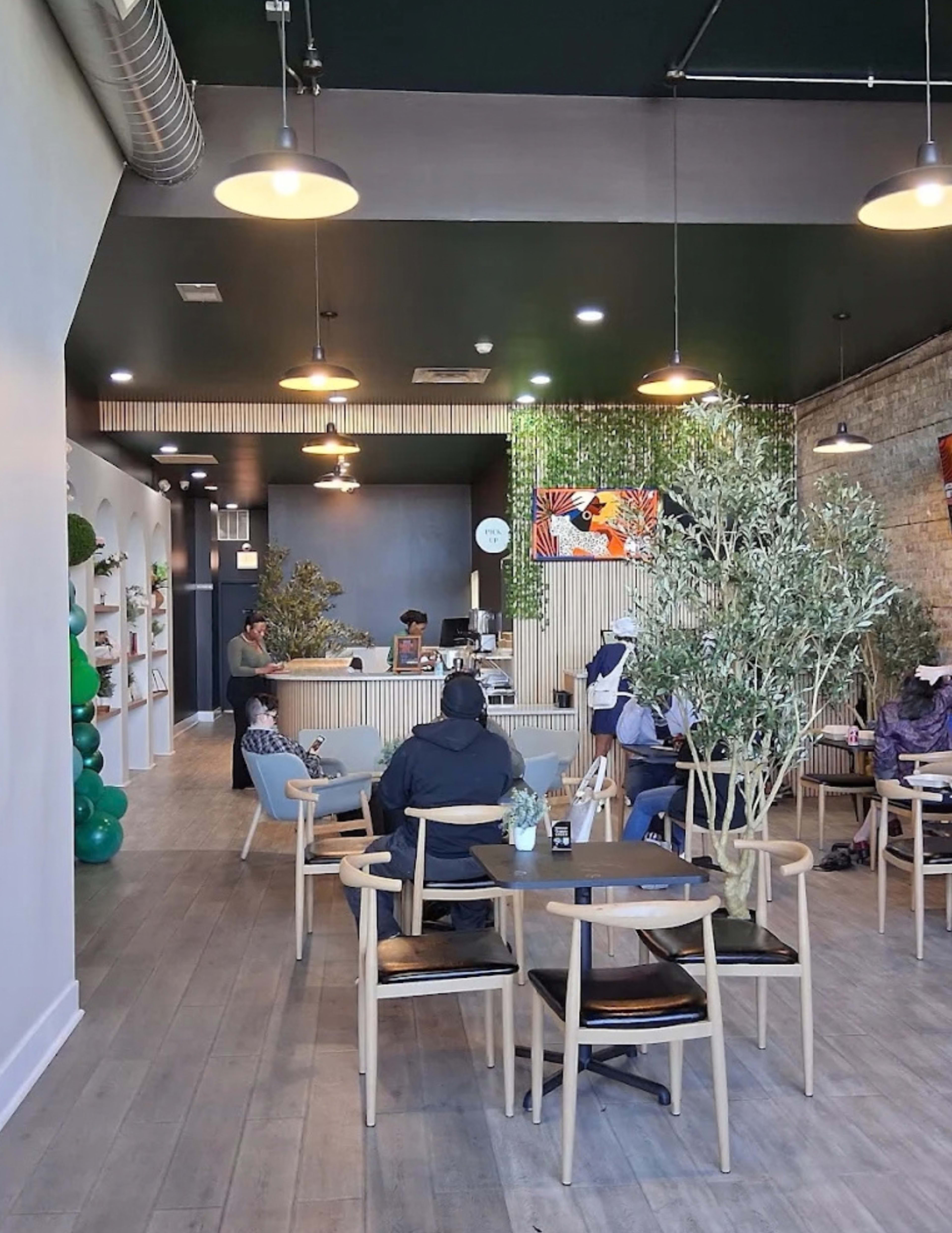 A modern cafe features a sleek interior with wooden flooring, green accents, and patrons seated at tables.