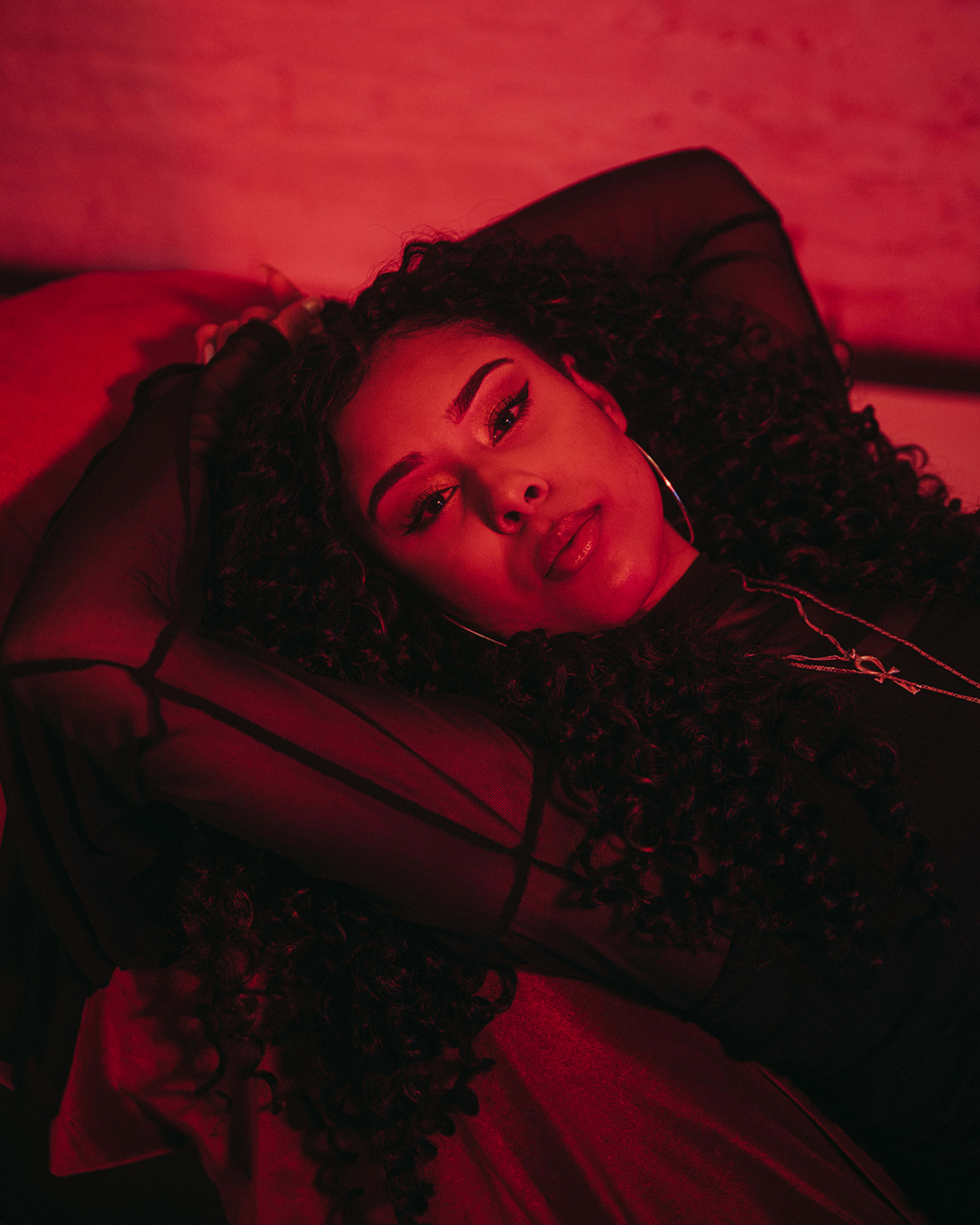 A woman with curly black hair in a portrait laying on a bed.