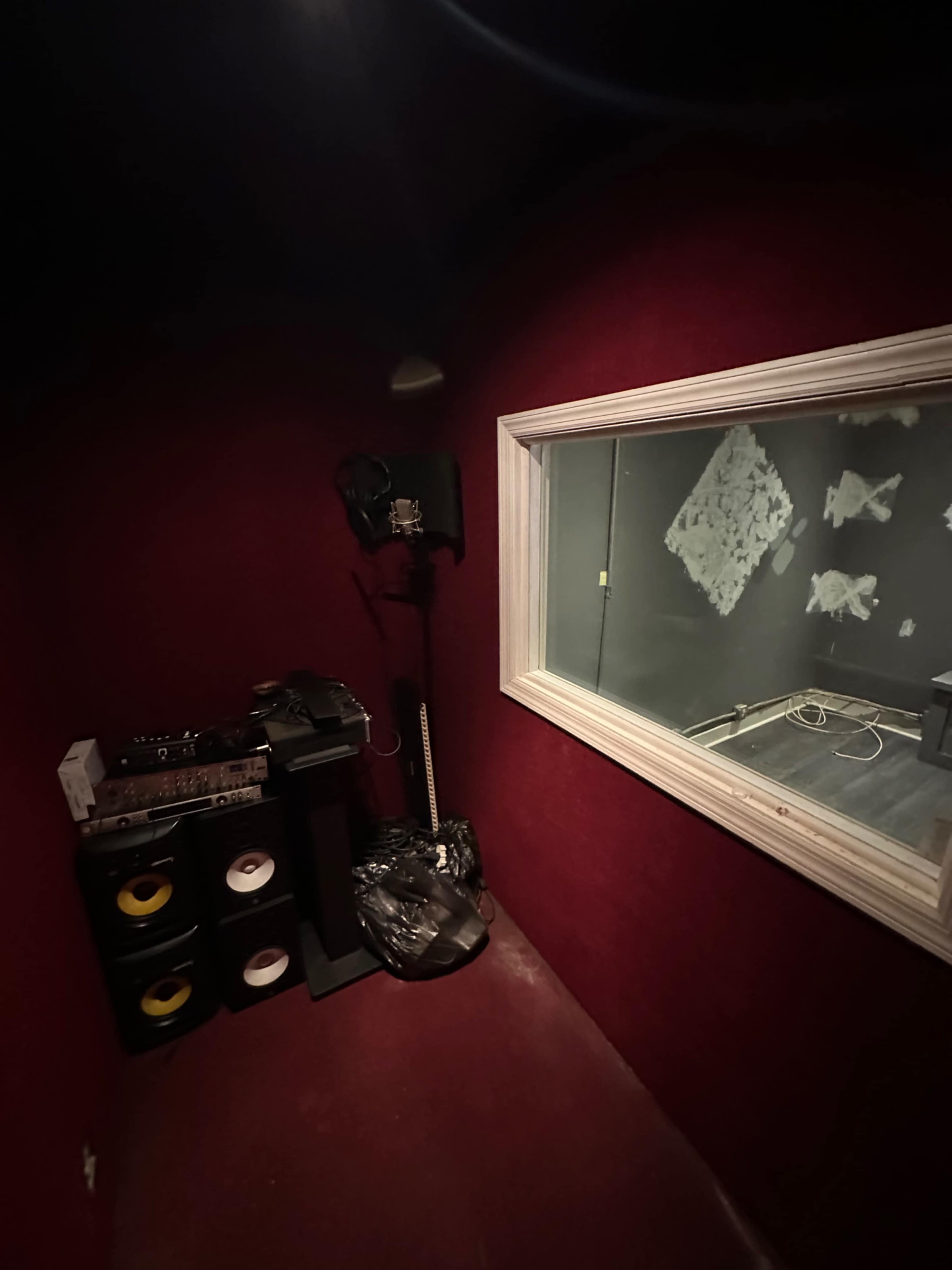 A small recording studio booth with soundproofed walls, a microphone stand, and audio equipment placed against the wall.