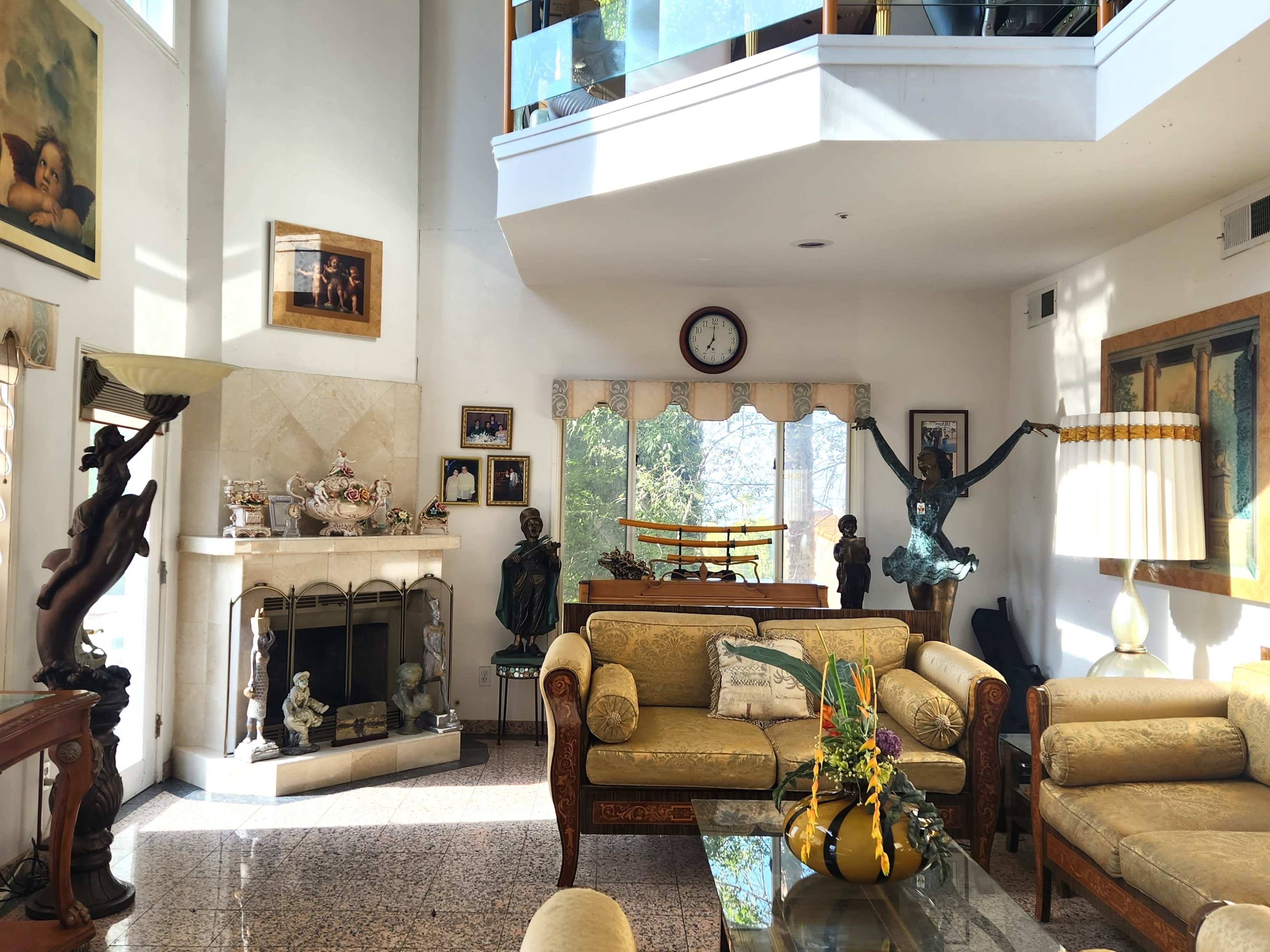 A sunny living room with a fireplace, elegant furniture, and various artworks displayed on the walls.