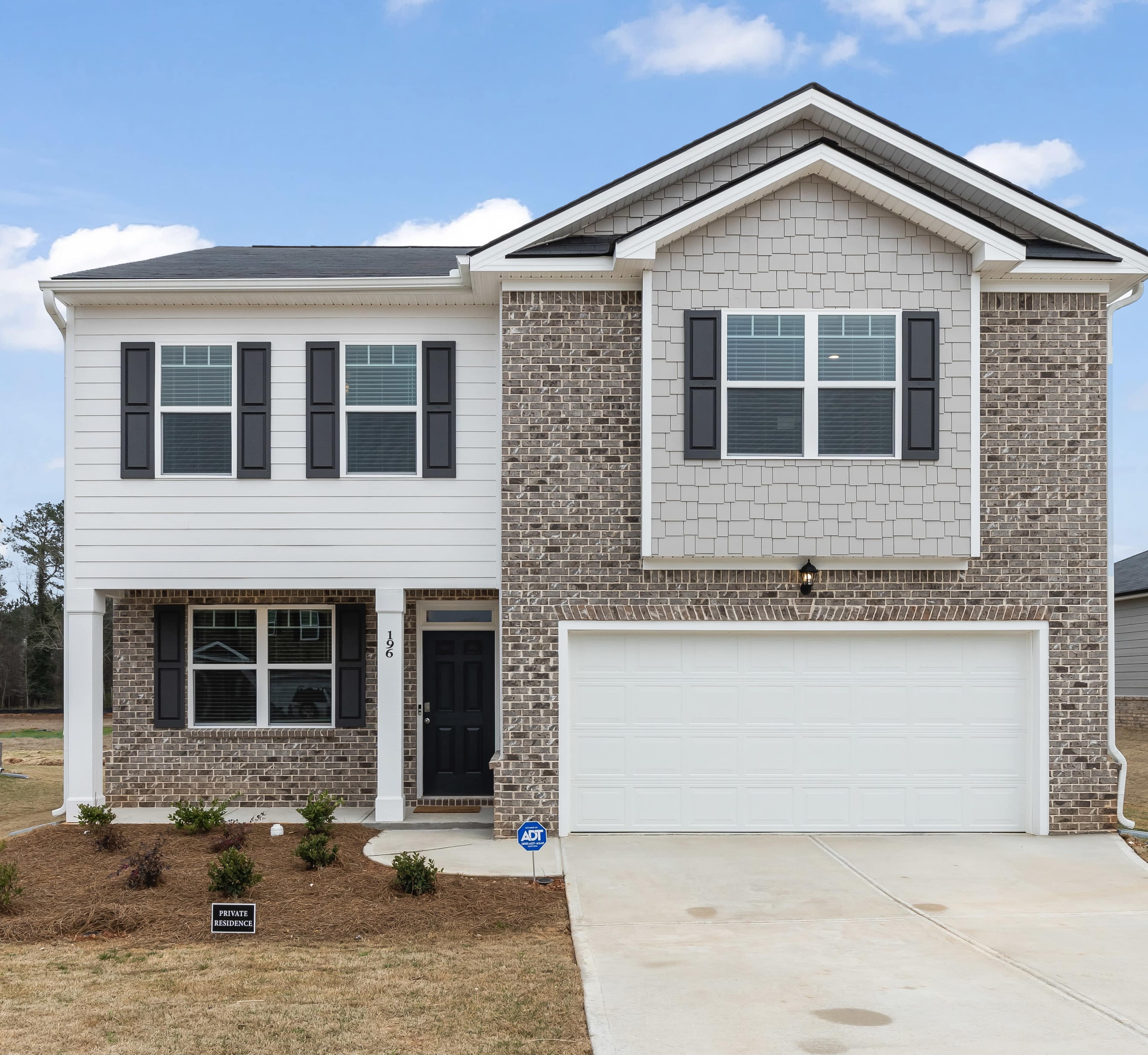A modern two-story house with a brick and siding exterior, featuring a front porch and an attached garage.