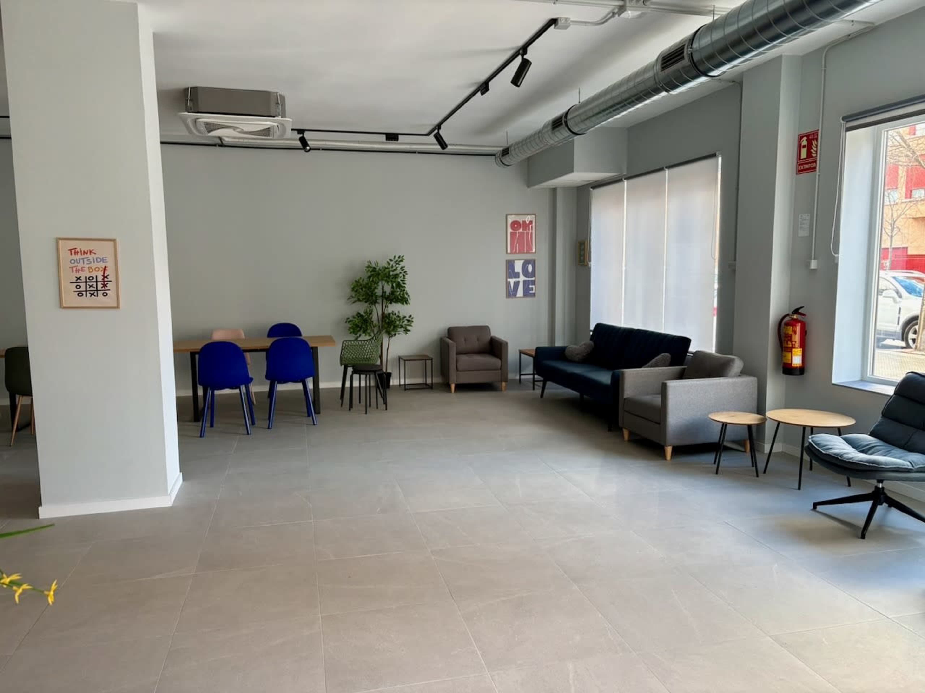 The image shows a modern, open space with seating arrangements, a small table, and a potted plant.