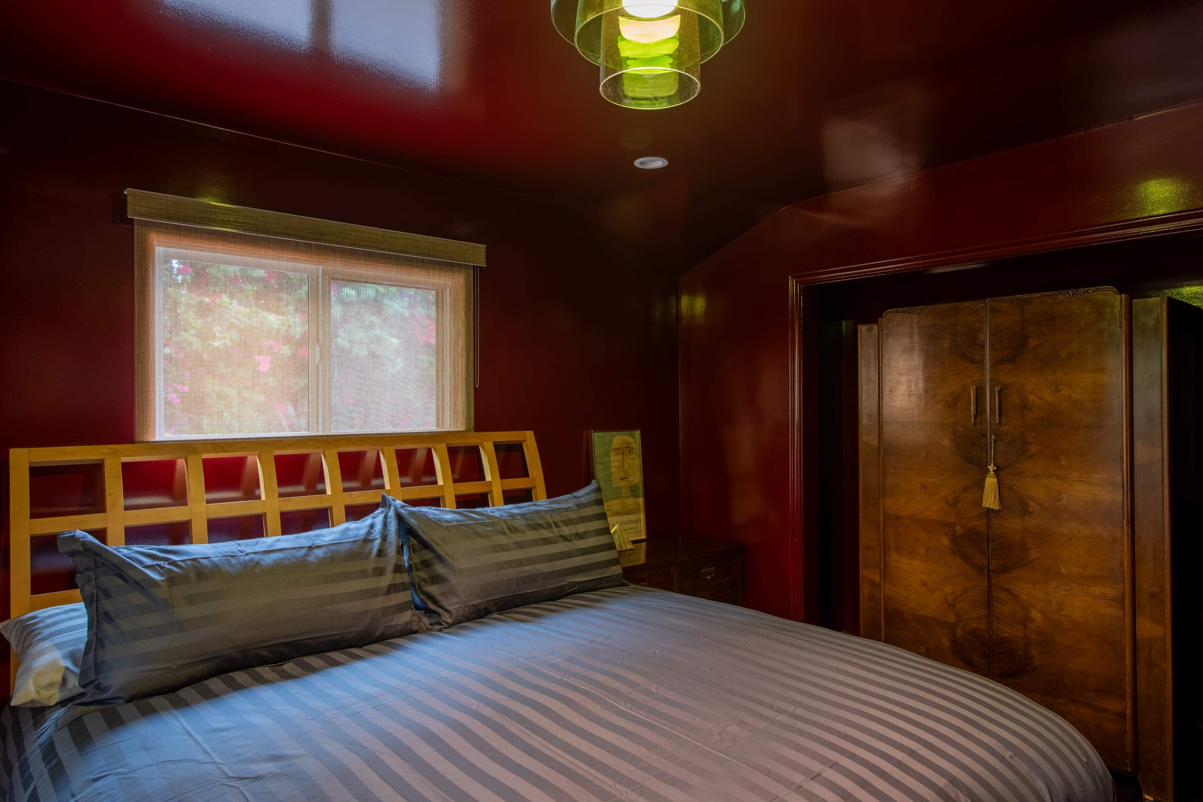 The image shows a bedroom with dark red walls, a wooden bed frame with a striped comforter, and a large wardrobe in the corner.