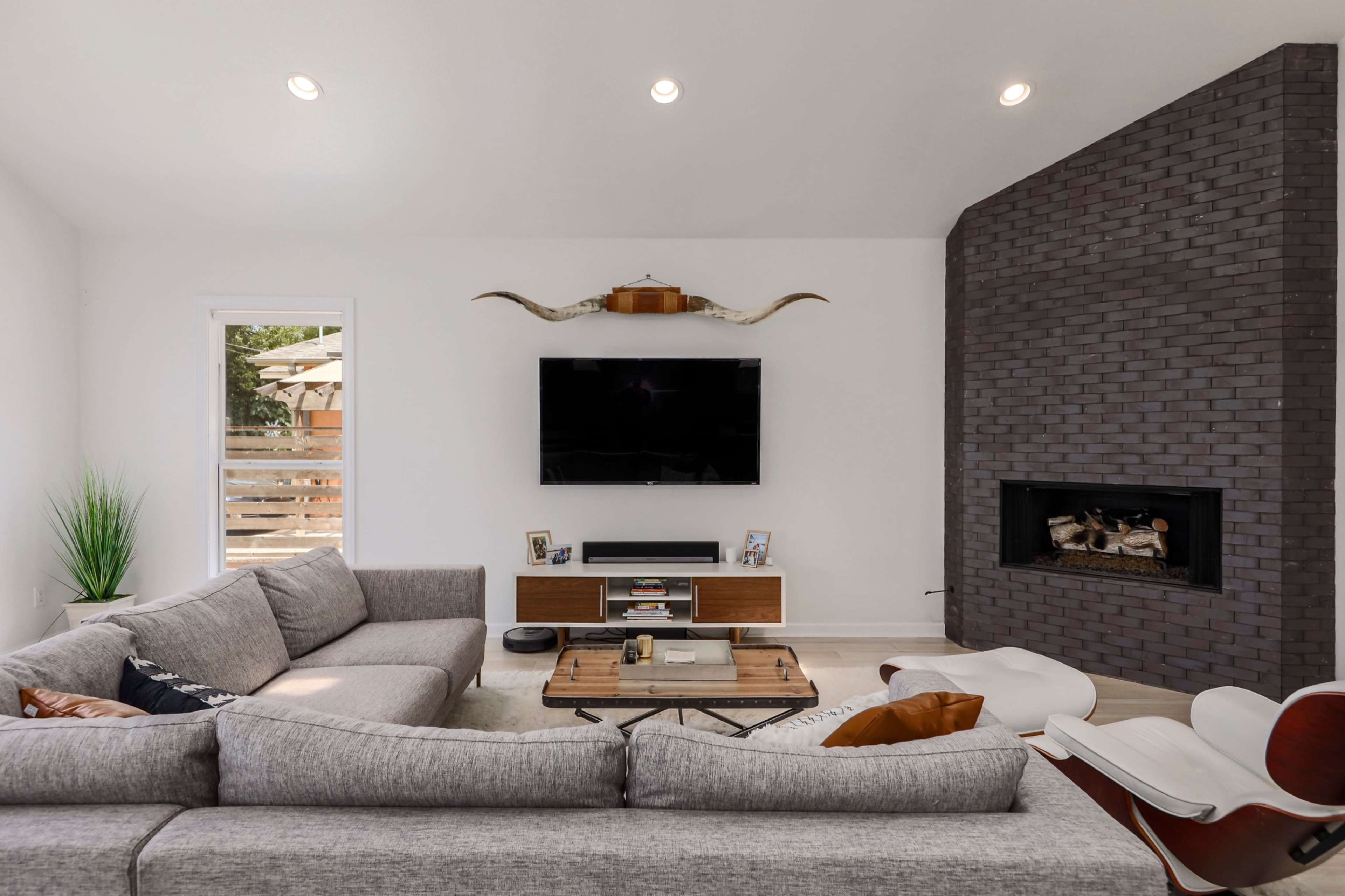 The living room features a sectional sofa, a wooden coffee table, a mounted television, and a fireplace with a dark brick wall.