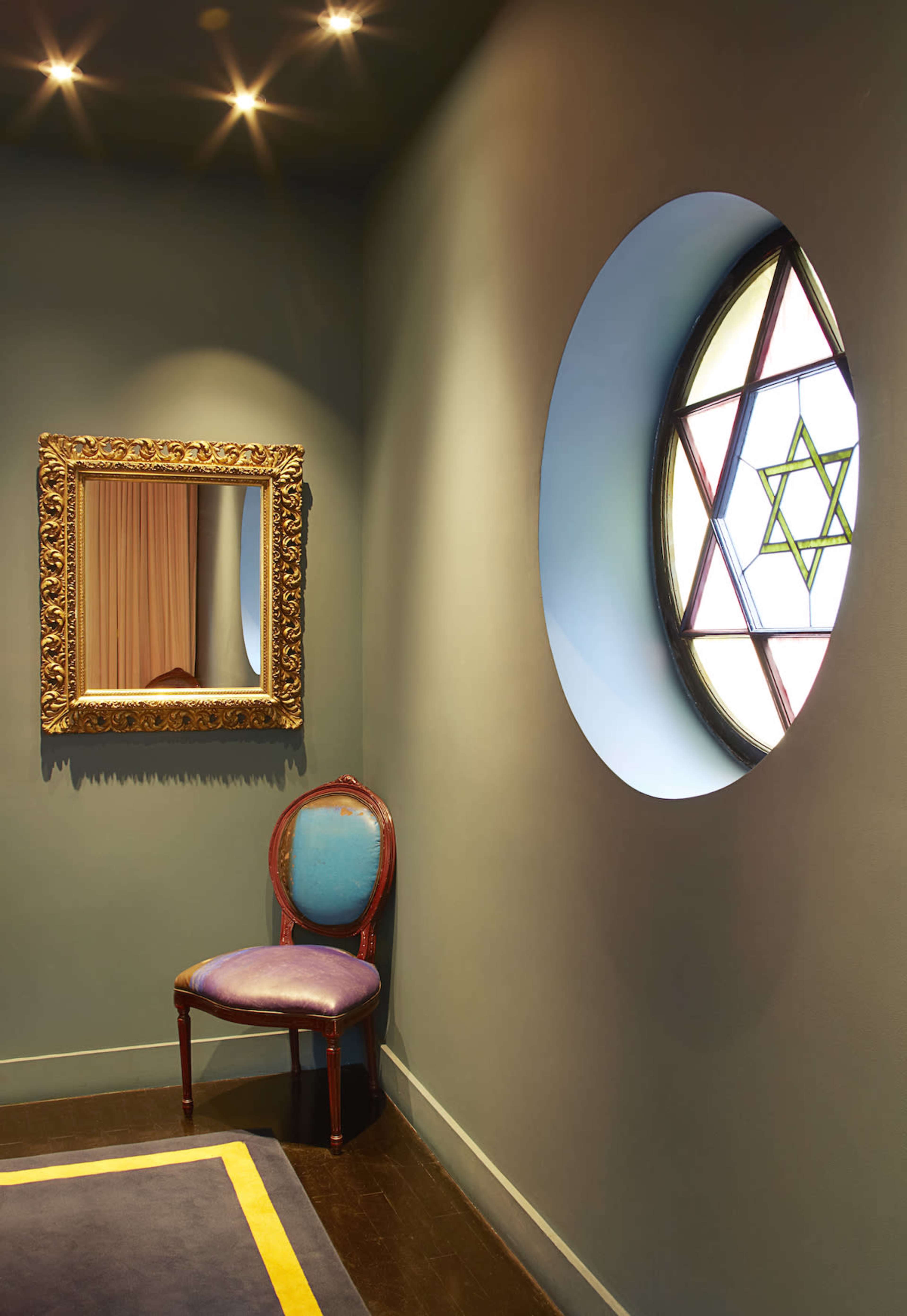 A corner of a room with a decorative mirror, a vintage chair, and a circular stained glass window depicting a Star of David.