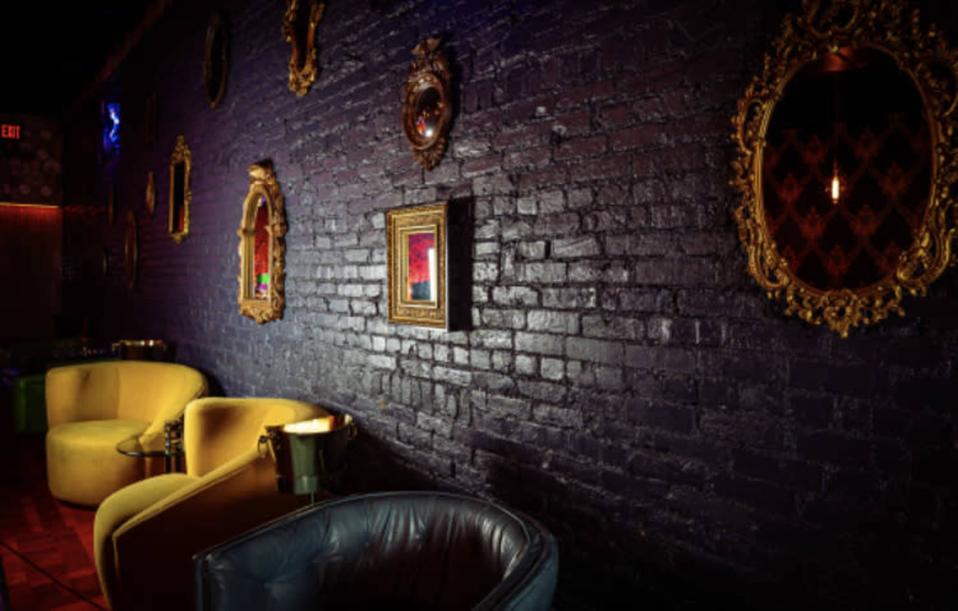 The scene features a dimly lit lounge with a dark brick wall adorned with ornate mirrors and vintage seating in yellow and blue.
