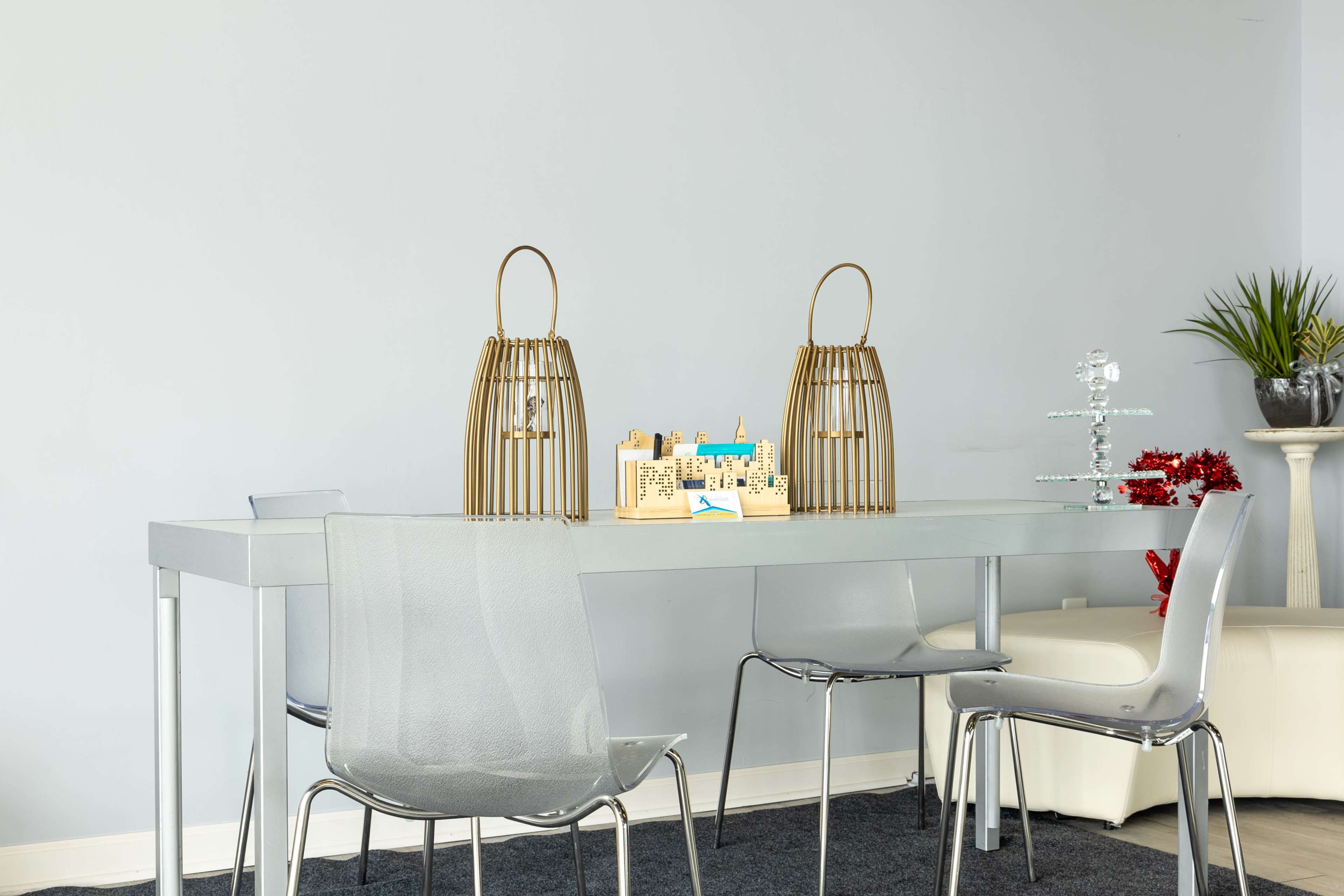 A modern dining table with two gold wire birdcage decorations and a wooden model of a city is set in a minimalist room with light gray walls.