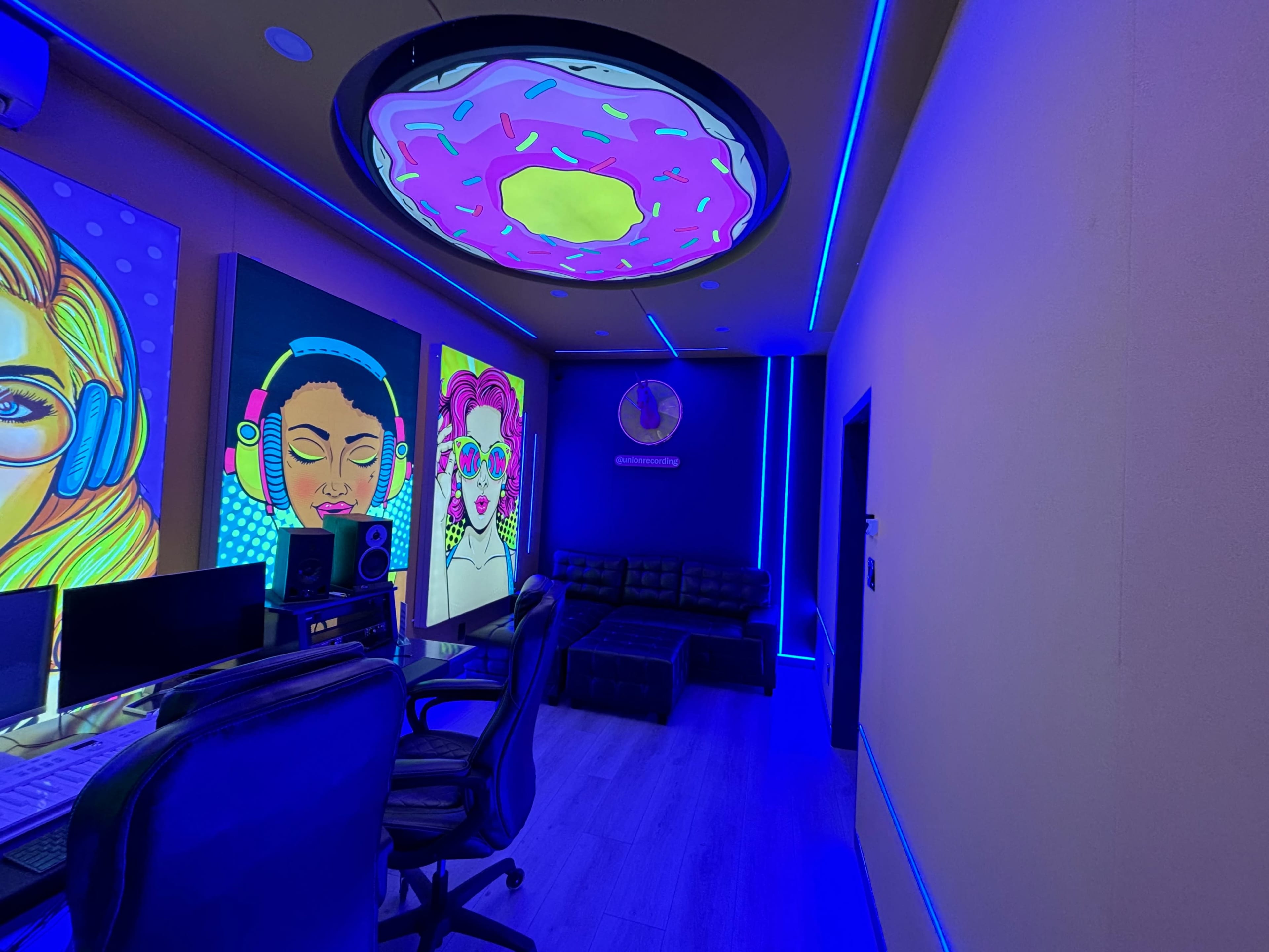 A modern room with colorful wall art, a donut-shaped ceiling light, and blue LED lighting along the walls.