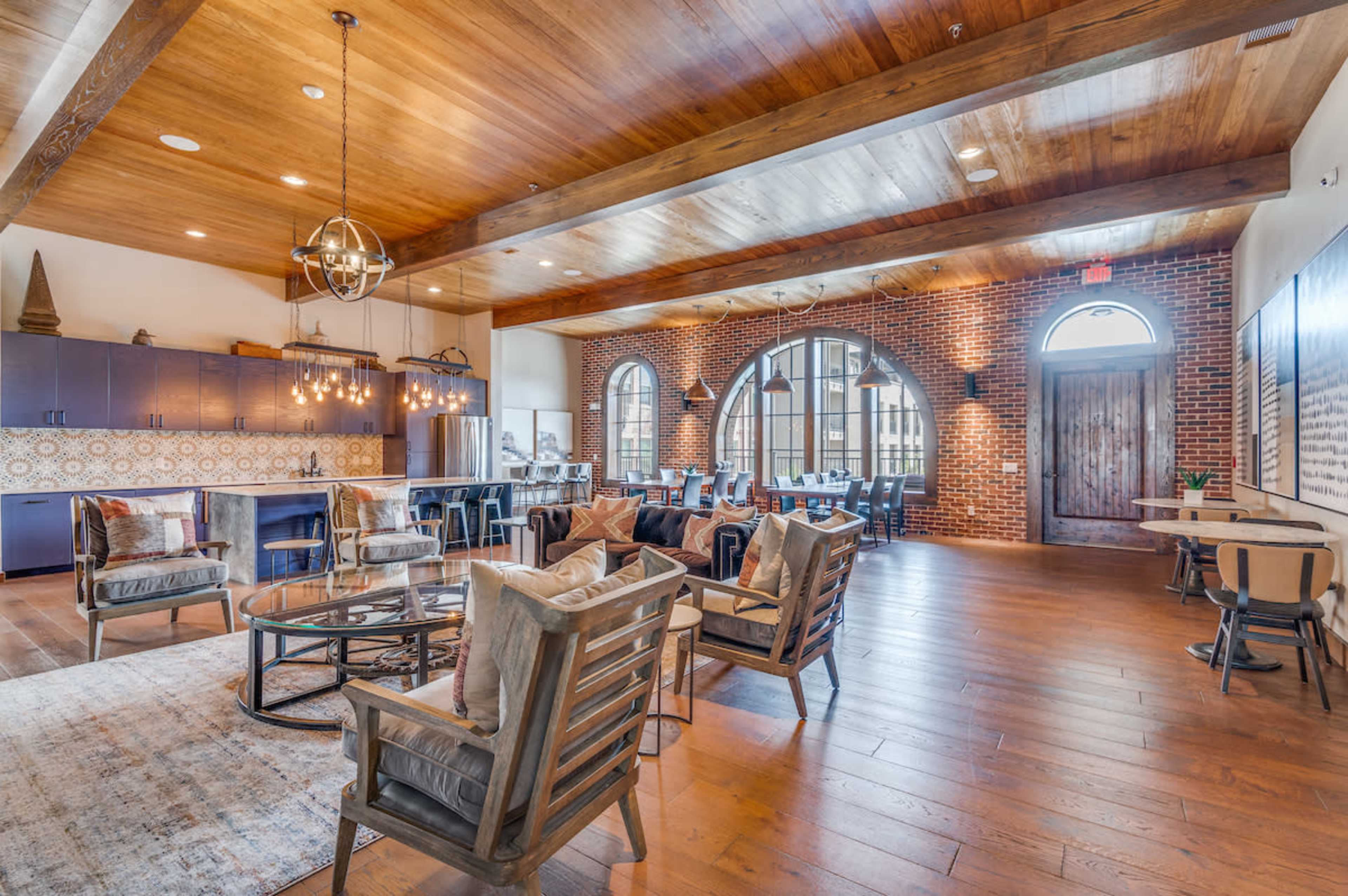 A spacious interior with wooden beams, a mix of seating arrangements, and large windows that illuminate a lounge area featuring brick walls and stylish decor.