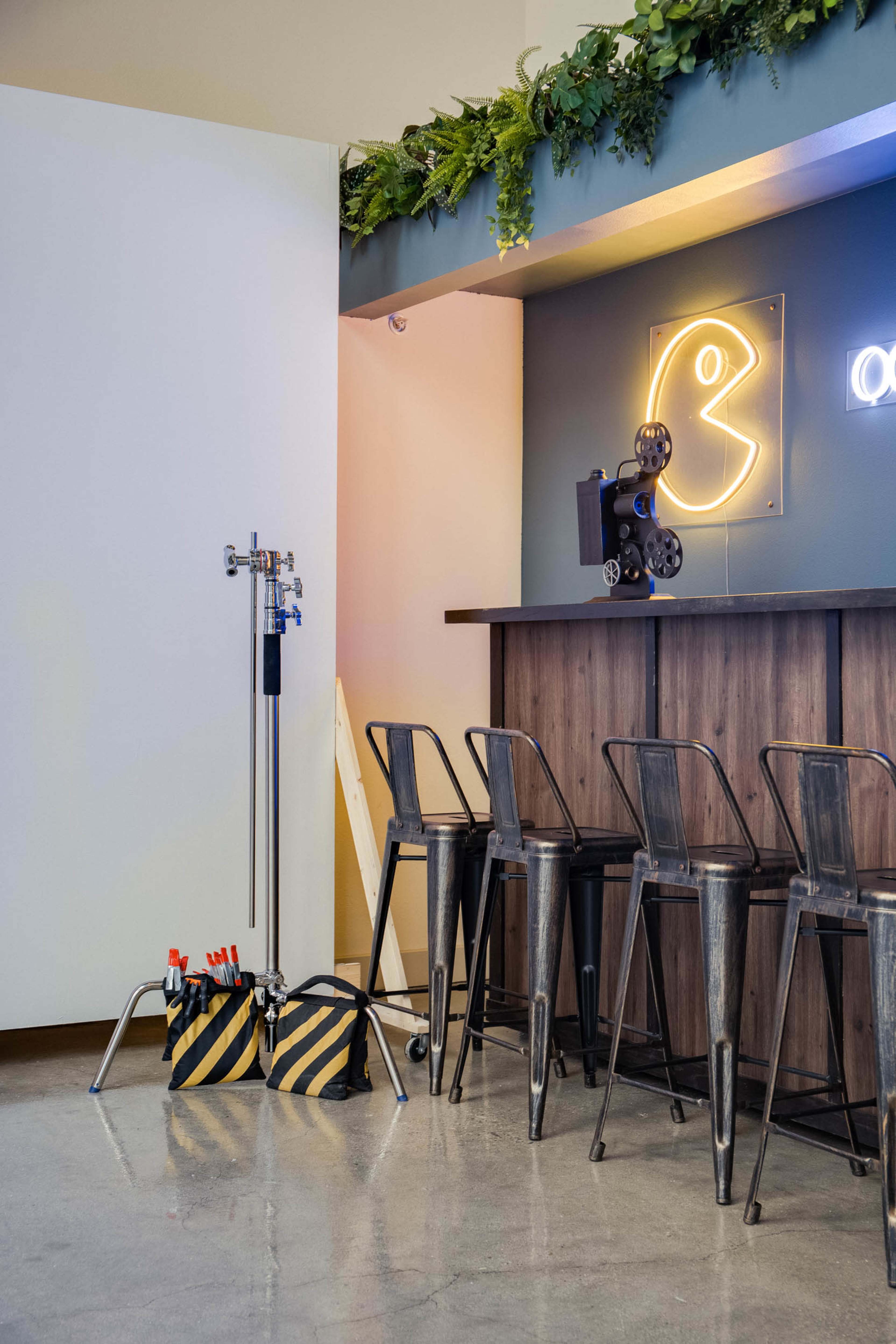 A modern bar area featuring metal stools, a wooden counter, and a neon light installation, alongside tool kits and equipment on the floor.