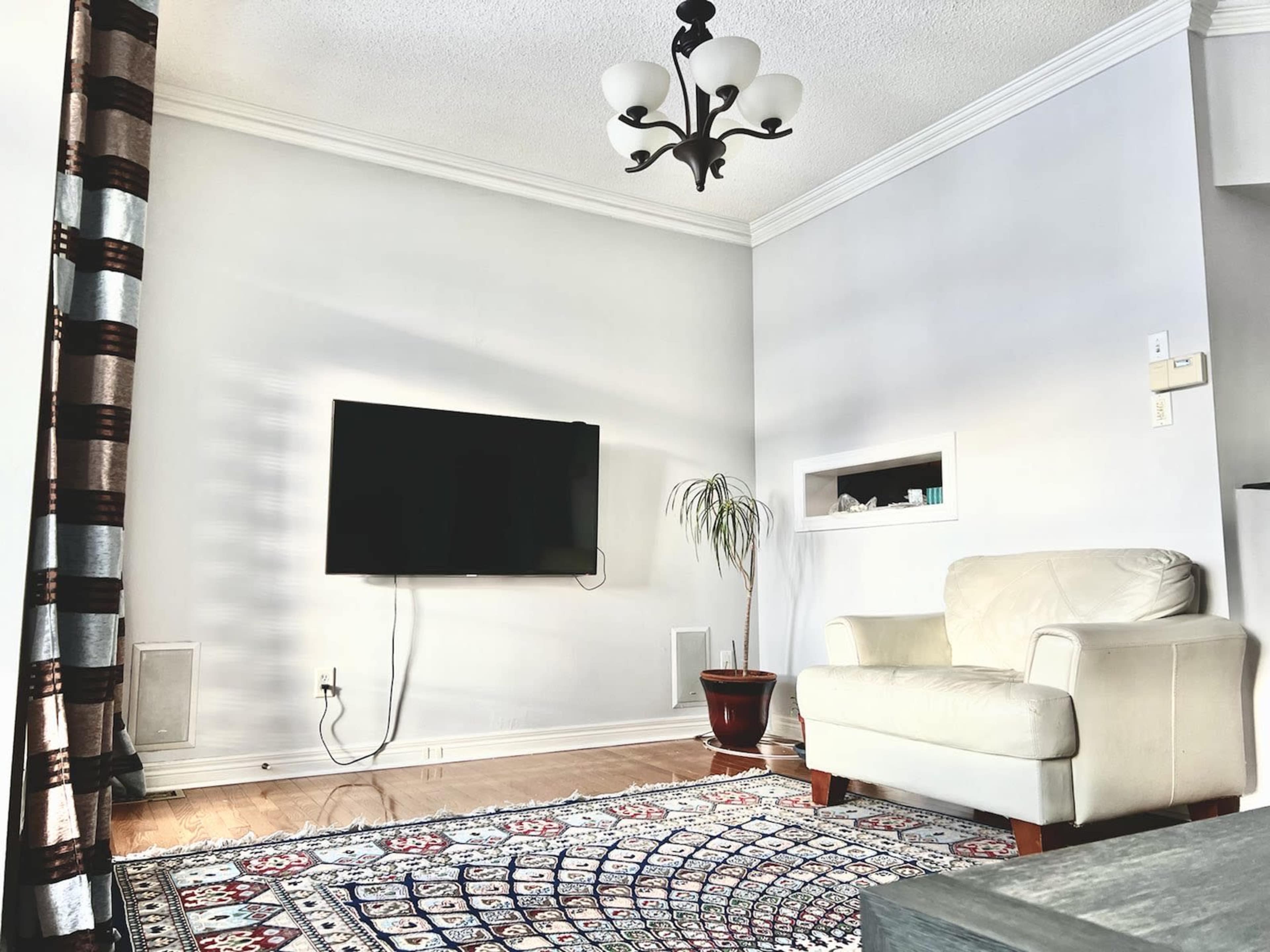 A modern living room featuring a white leather armchair, a mounted flat-screen TV, and a decorative area rug on wooden flooring.