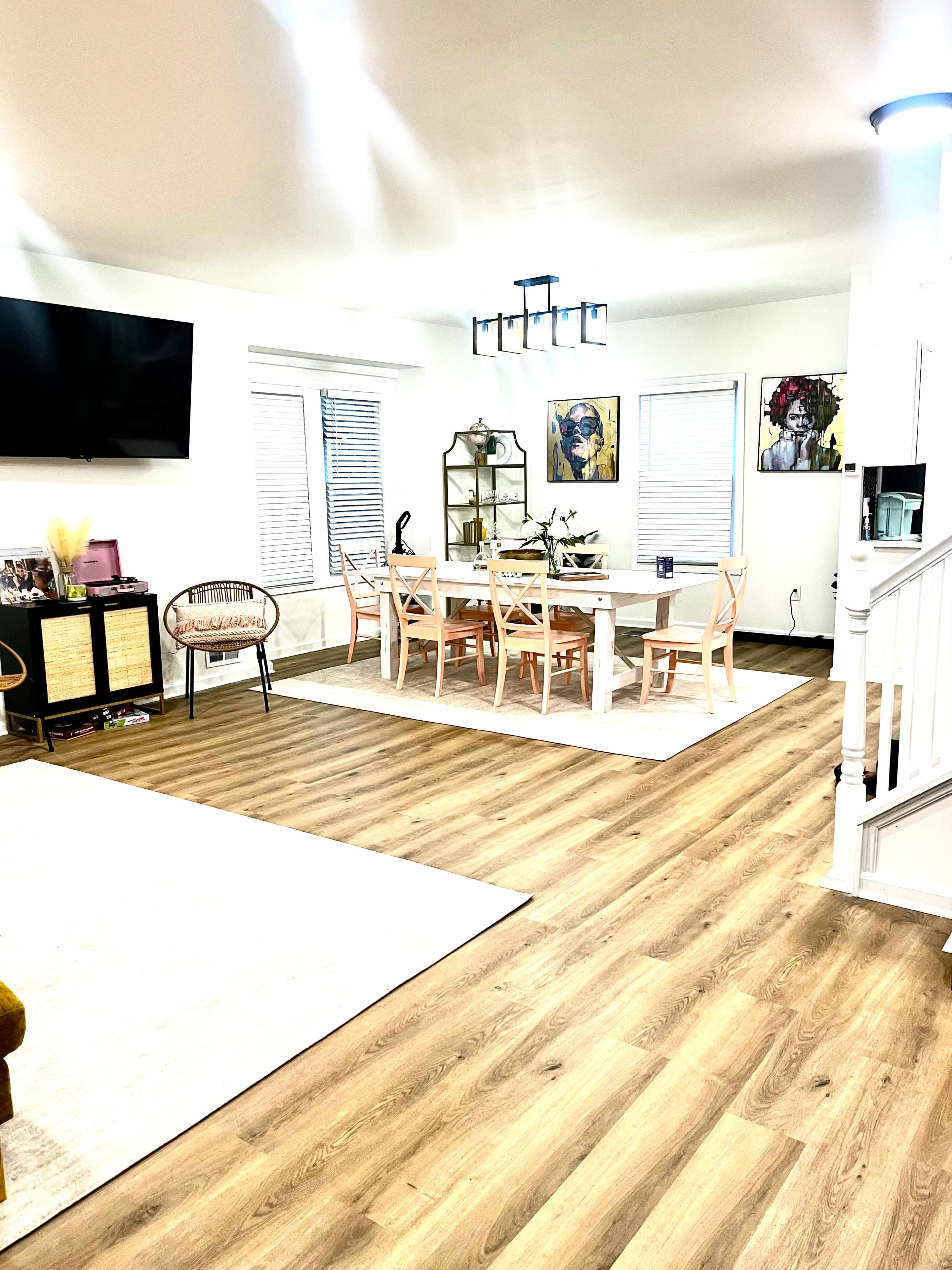 A modern living space features a dining area with a table surrounded by chairs, a seating area with a television, and art displayed on the walls.