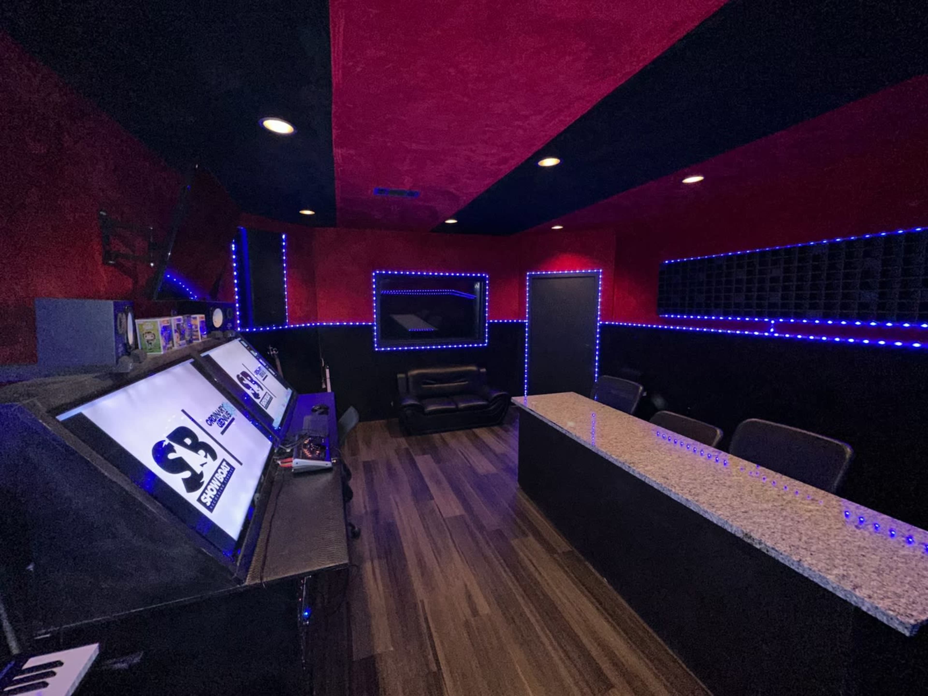 The image shows a modern recording studio with a sleek black and red color scheme, featuring LED lighting and a granite countertop.