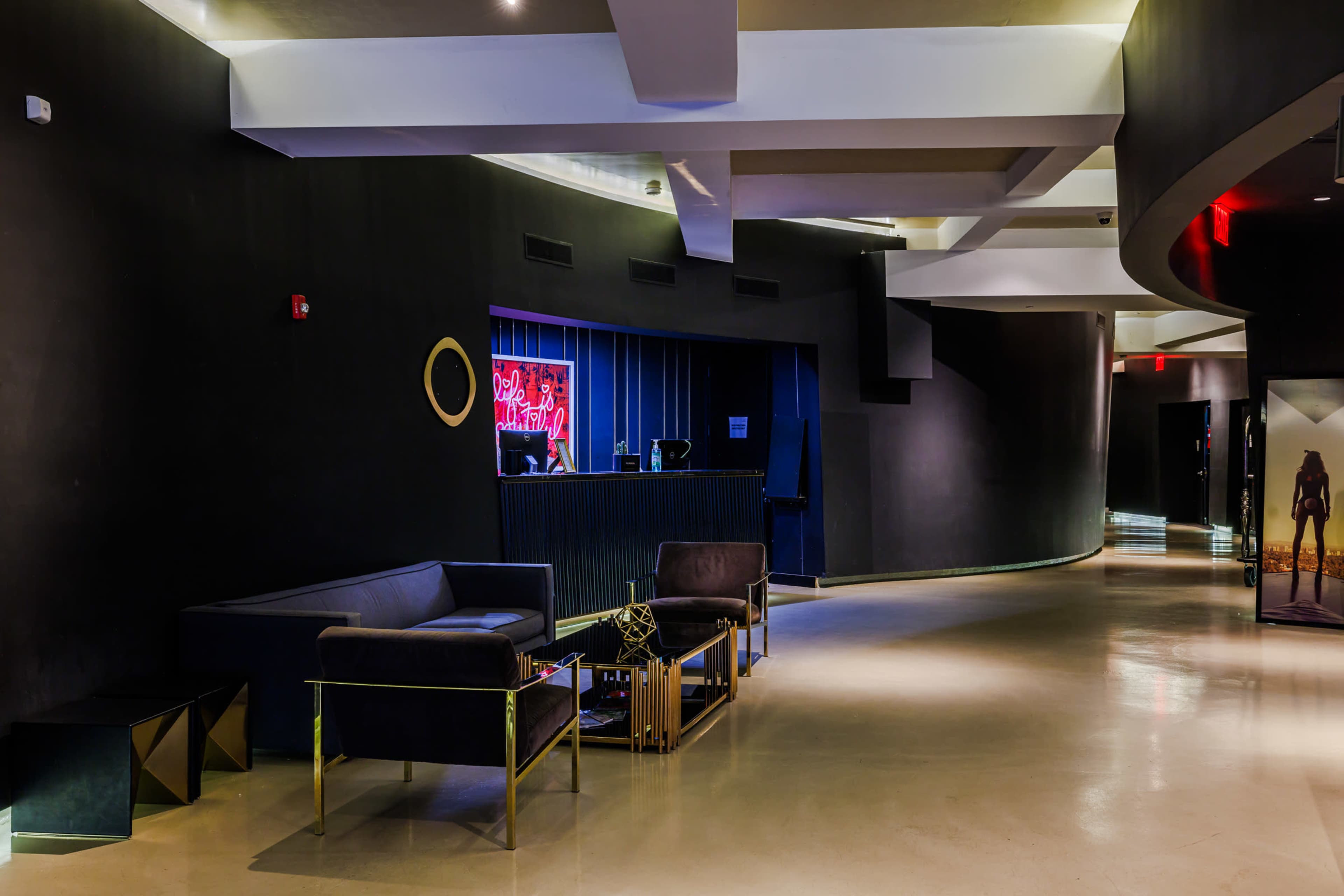 The image shows a modern, dimly lit lobby with a sleek design featuring a reception desk and contemporary seating arrangements.