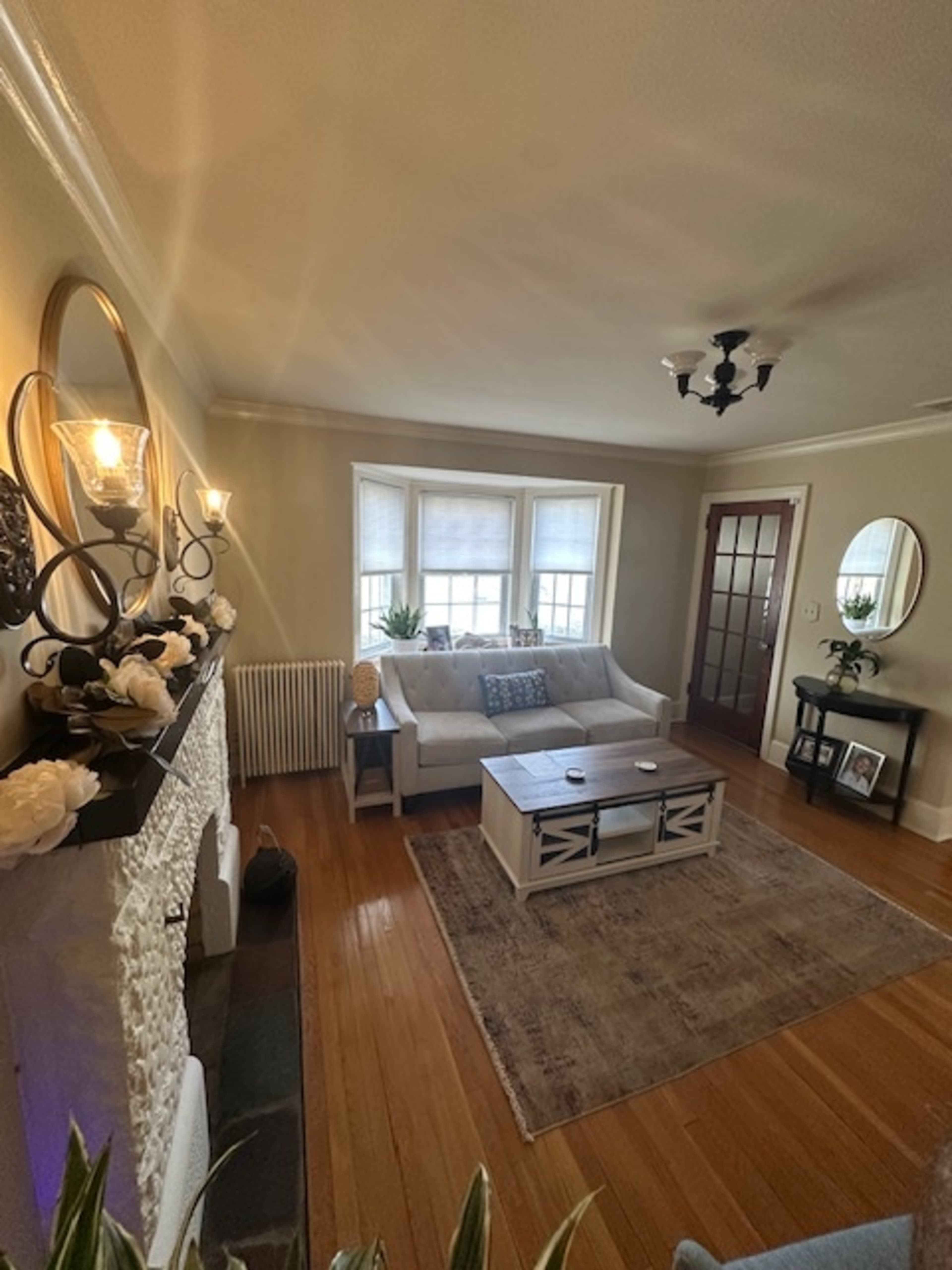 The image shows a cozy living room with a gray sofa, a coffee table in front, and a window with light coming through, along with decorative items and a door leading to another room.