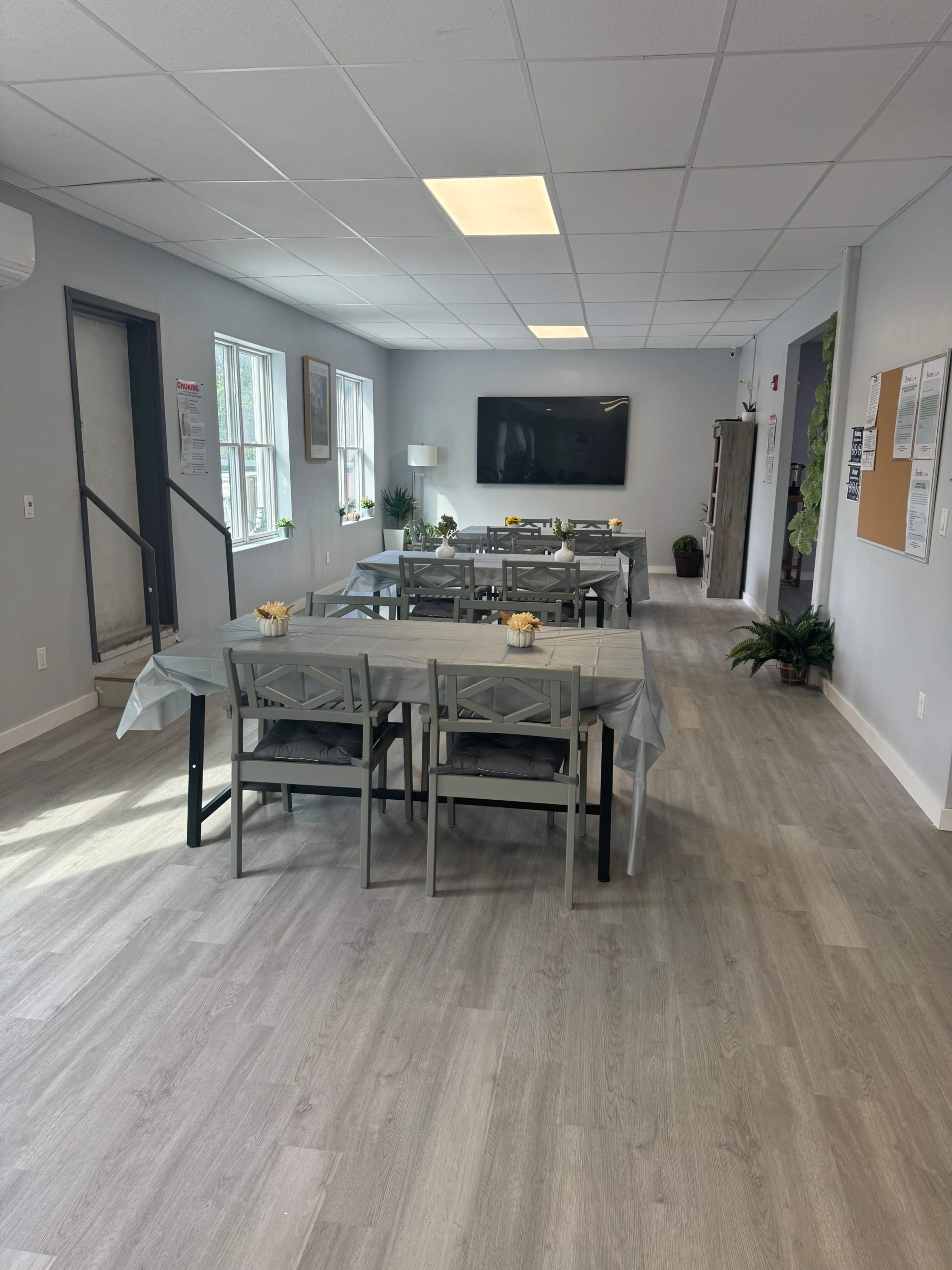 The image shows a well-lit room with several tables set up for dining, featuring chairs and a television on one wall.