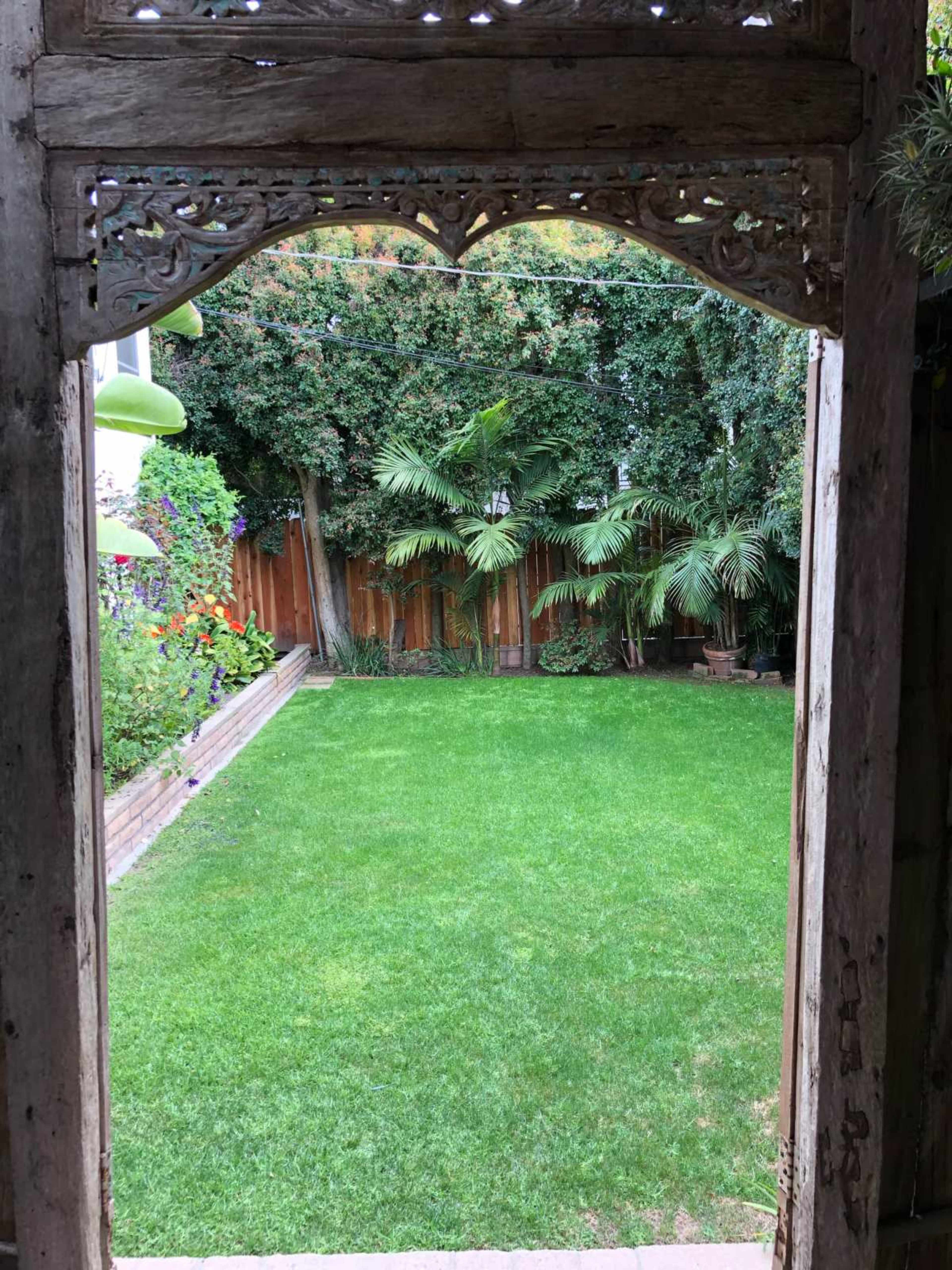 A wooden archway frames a neatly maintained green lawn surrounded by lush foliage and wooden fencing.